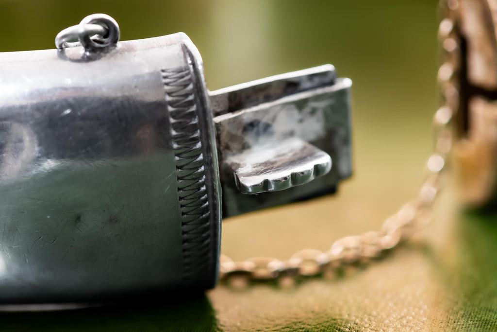 Close-up of a wide, vintage 1969 Birmingham sterling silver hinged bangle with intricate botanical engravings and a safety chain, resting beautifully on a vintage leather-bound book.