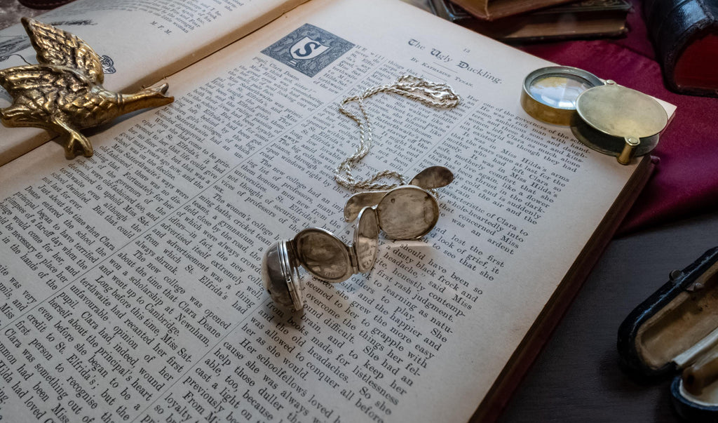 An antique silver ribbed sphere locket resting on an open vintage book. The first image shows the locket closed as a solid ball. The second image shows the locket mechanically unfolded into an accordion of six circular picture frames, lying across the text.