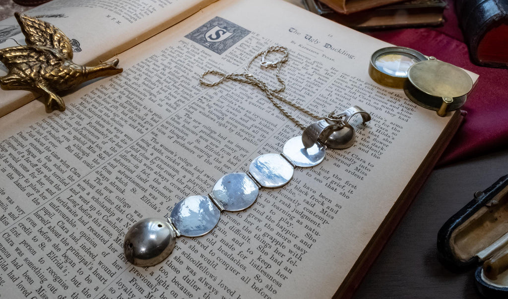 An antique silver ribbed sphere locket resting on an open vintage book. The first image shows the locket closed as a solid ball. The second image shows the locket mechanically unfolded into an accordion of six circular picture frames, lying across the text.