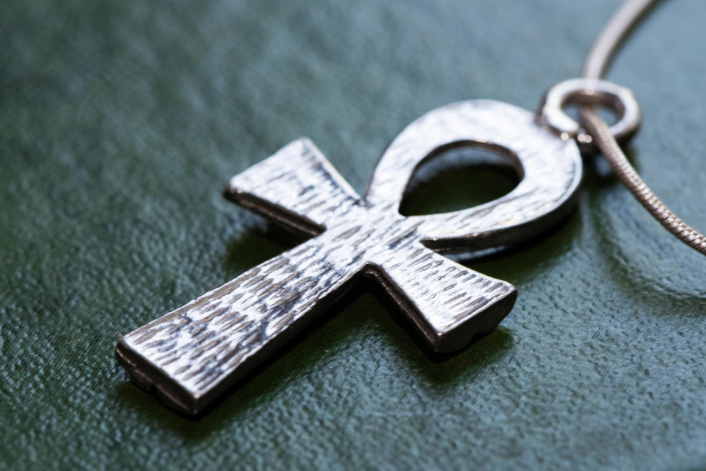 Textured sterling silver Ankh Egyptian cross pendant suspended on a fluid vintage silver snake chain. The everyday armor gothic jewelry rests on a dark green grimoire book.