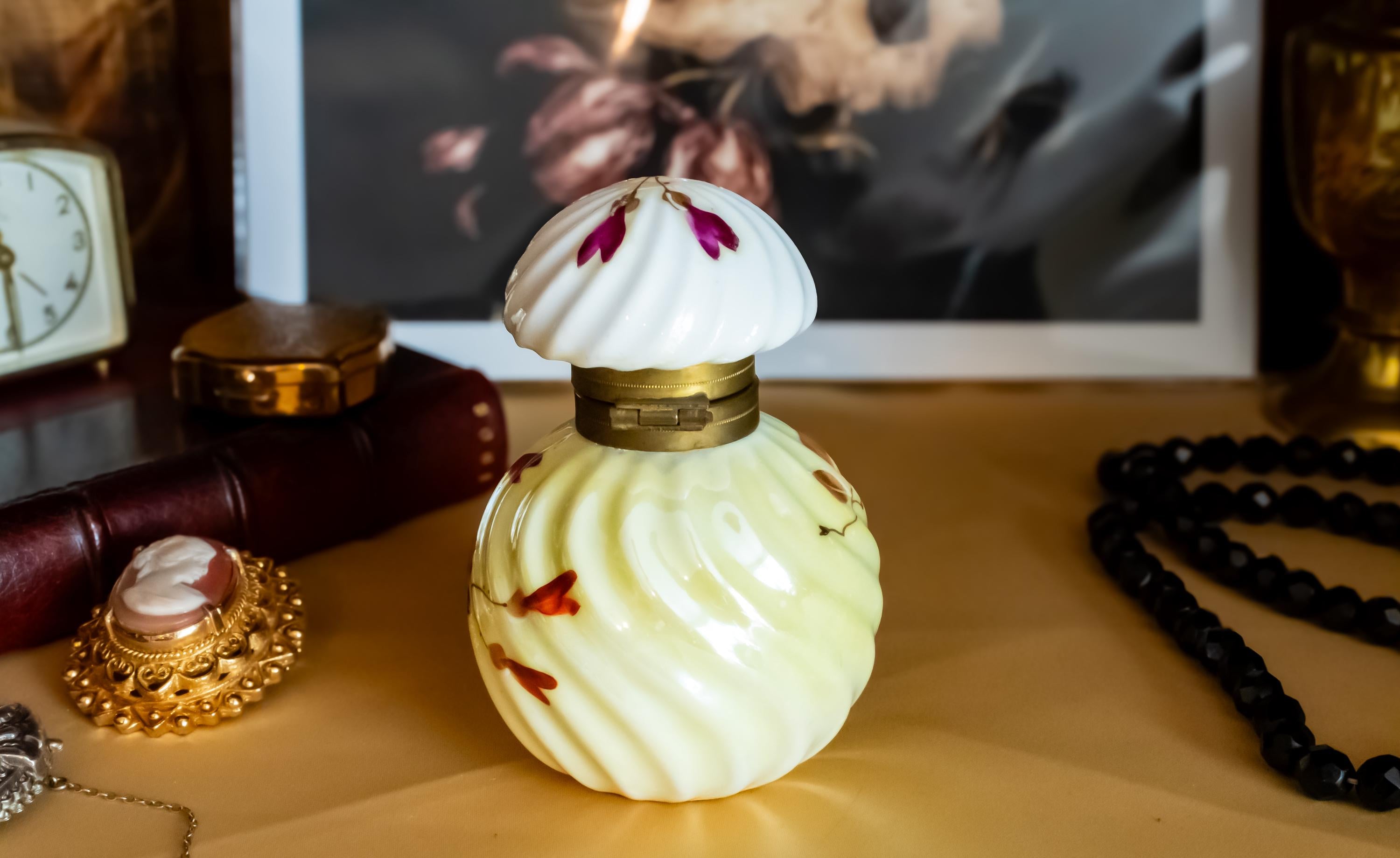 Antique pale yellow ribbed glass inkwell with hand-painted Victorian floral motifs in purple and red. The desk decor features a brass collar and a swirled white glass stopper, sitting on a writer's desk.