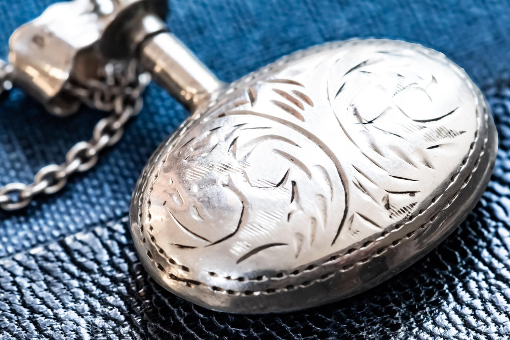 Miniature Victorian sterling silver perfume vial necklace. The antique poison bottle pendant features intricate botanical engravings and an unscrewed threaded cap with the original silver dauber wand attached