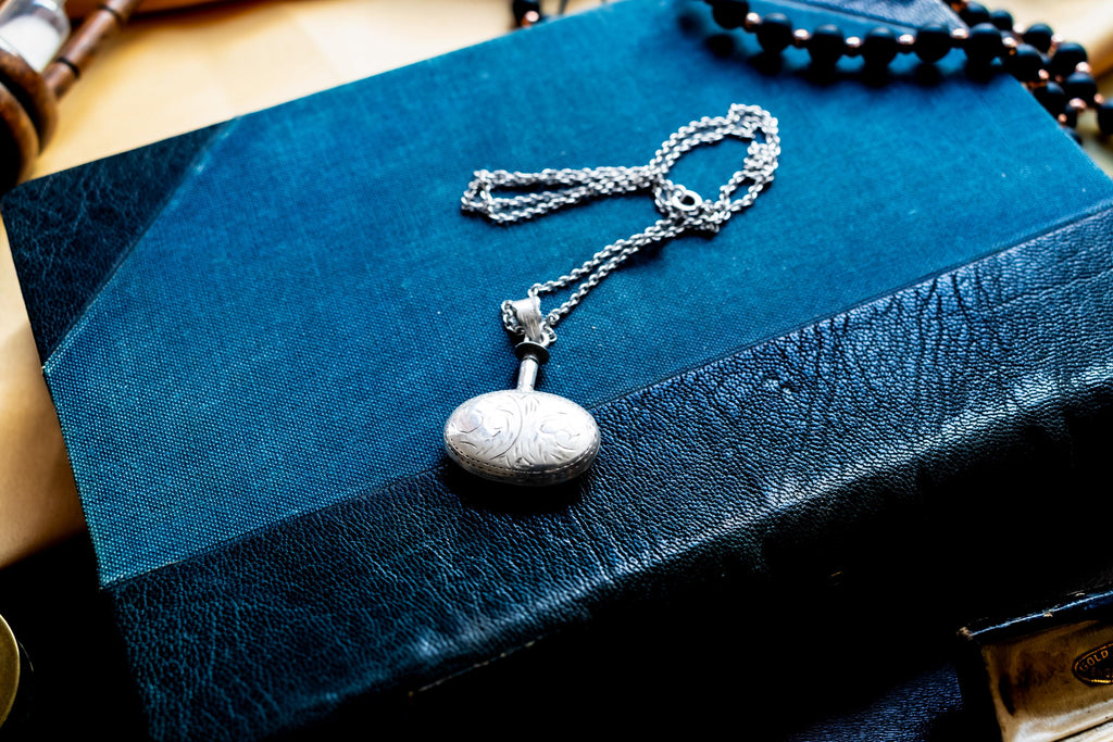 Miniature Victorian sterling silver perfume vial necklace. The antique poison bottle pendant features intricate botanical engravings and an unscrewed threaded cap with the original silver dauber wand attached