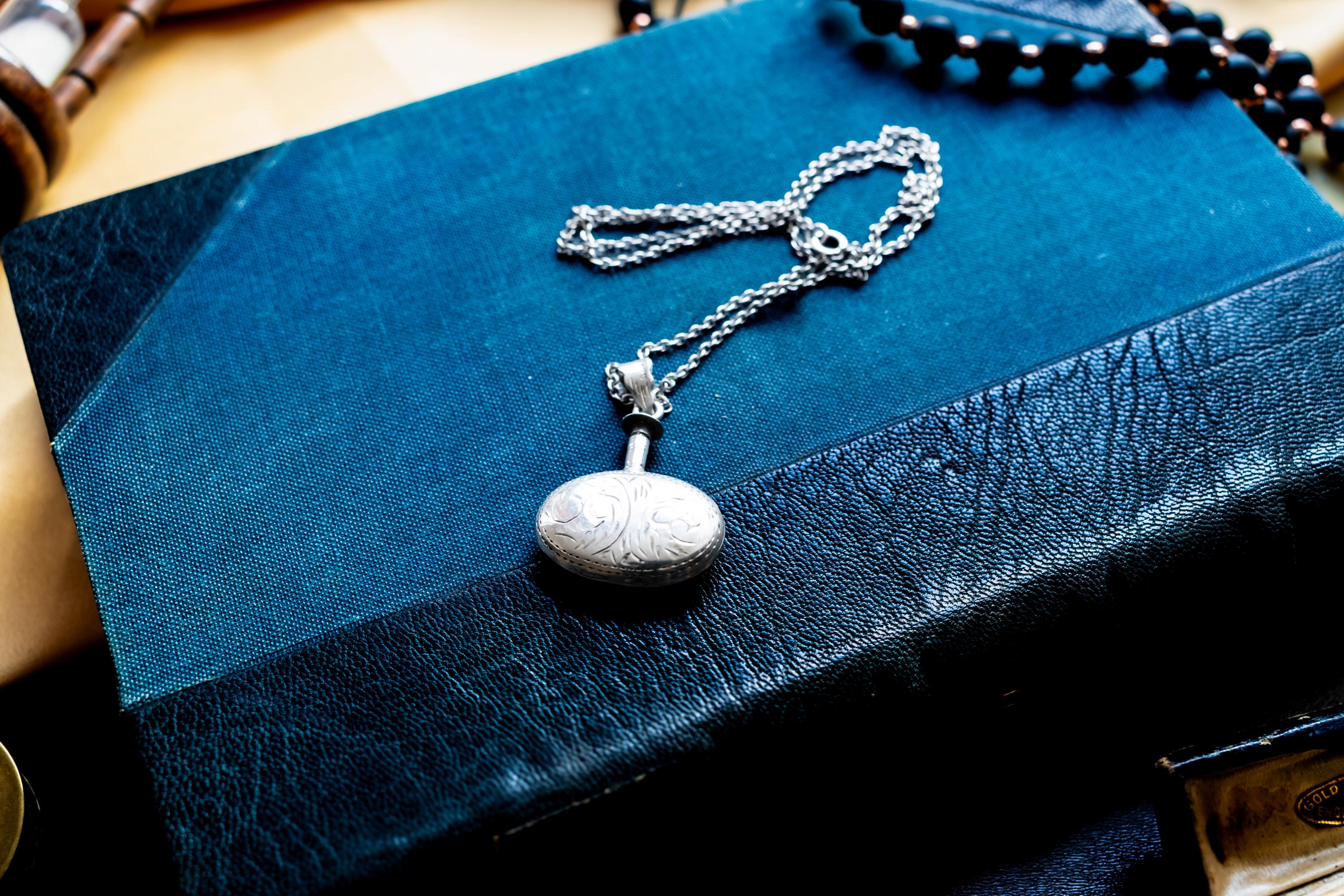 Miniature Victorian sterling silver perfume vial necklace. The antique poison bottle pendant features intricate botanical engravings and an unscrewed threaded cap with the original silver dauber wand attached