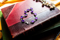 A silver bracelet featuring oval-shaped, deep purple amethyst gemstones set in polished metal links. The bracelet is draped on a red leather bound vintage book.