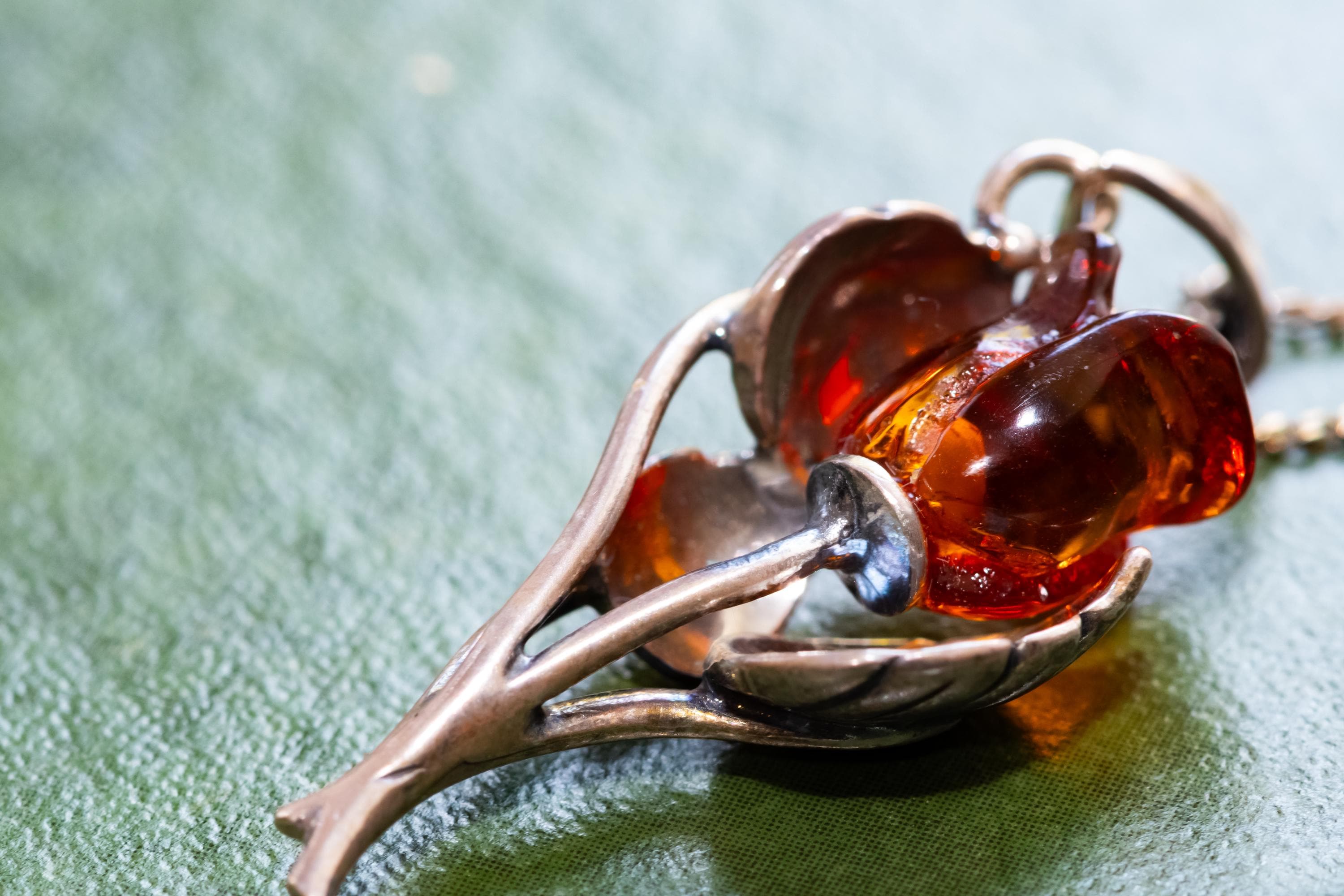 A vintage 925 sterling silver necklace featuring a carved Baltic amber rose pendant, beautifully staged resting on the cover of an antique green book with a dark carved brooch in the background.