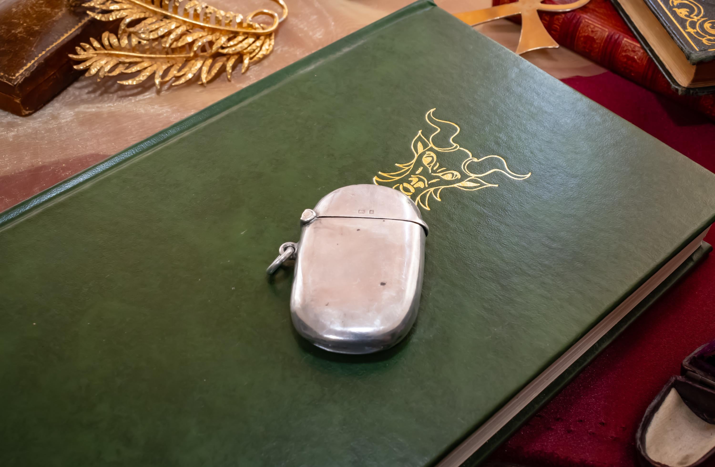 Antique 1906 Edwardian sterling silver vesta case by Thomas Bishton, shown closed and open on a vintage book next to a brass magnifying glass.