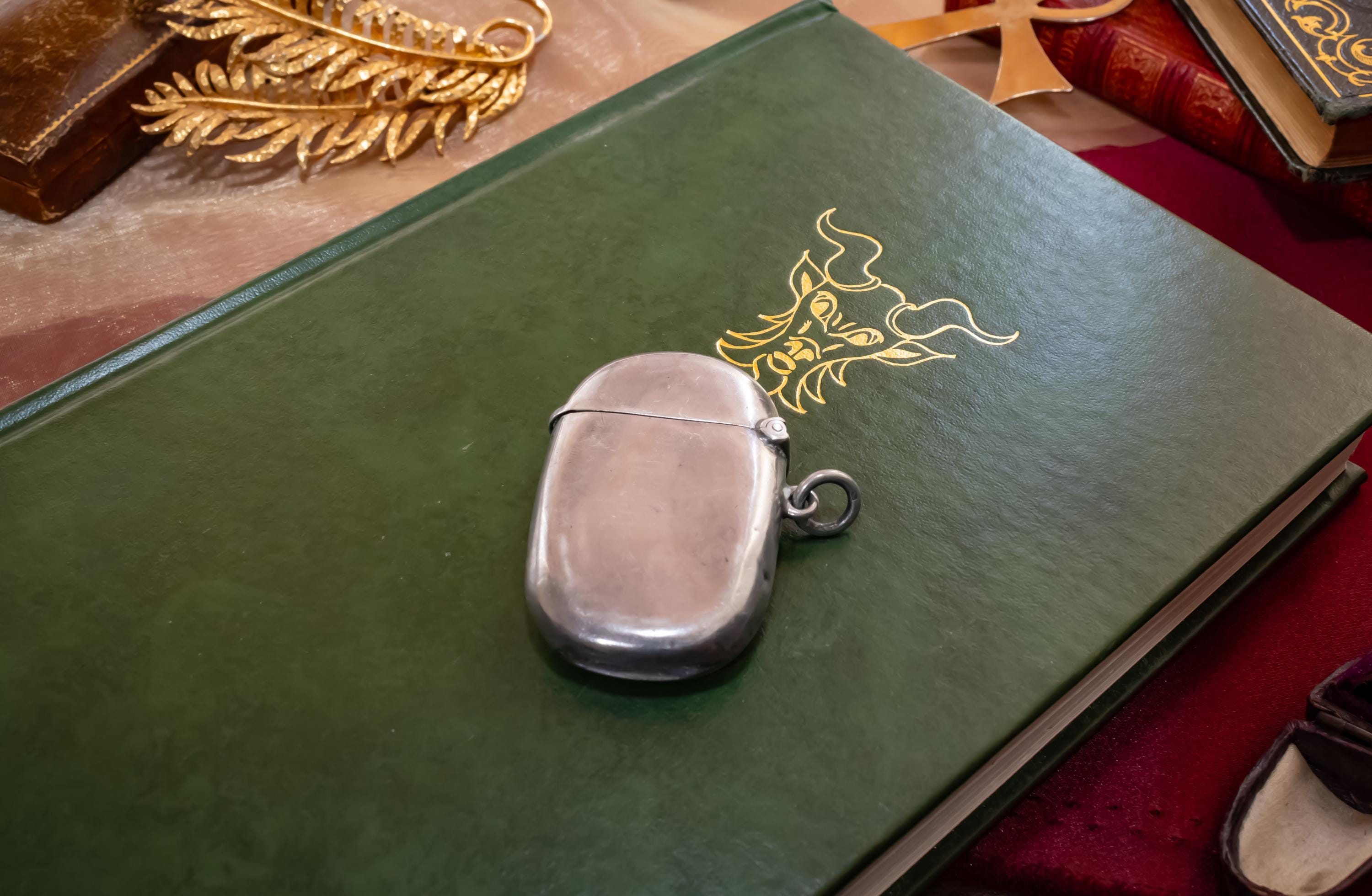 Antique 1906 Edwardian sterling silver vesta case by Thomas Bishton, shown closed and open on a vintage book next to a brass magnifying glass.