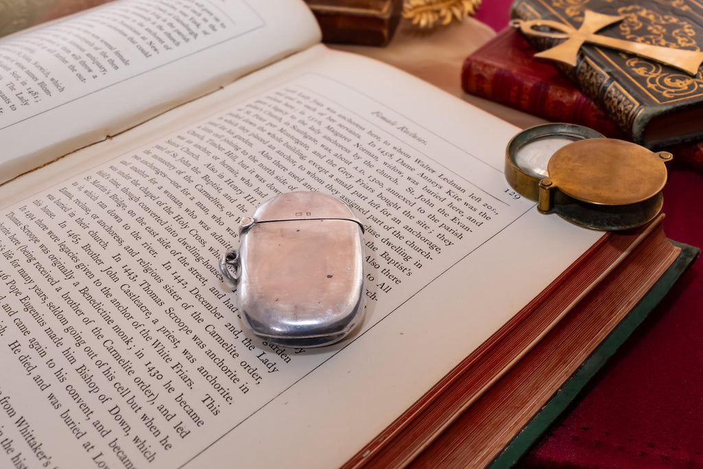Antique 1906 Edwardian sterling silver vesta case by Thomas Bishton, shown closed and open on a vintage book next to a brass magnifying glass.