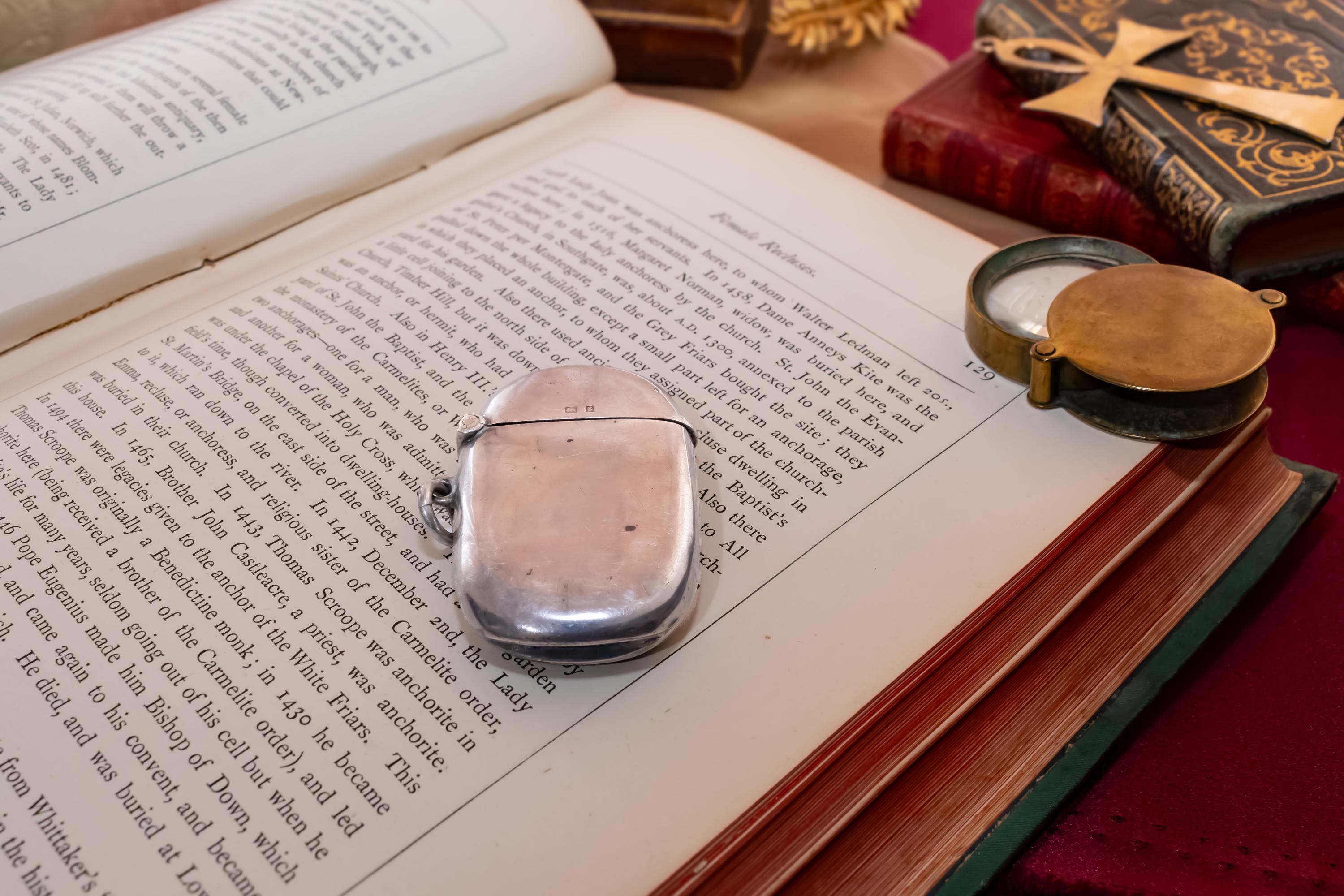 Antique 1906 Edwardian sterling silver vesta case by Thomas Bishton, shown closed and open on a vintage book next to a brass magnifying glass.
