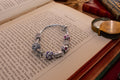 Authentic Pandora sterling silver snake chain bracelet loaded with nine various charms including a letter M and purple enamel beads, resting on an open antique book.
