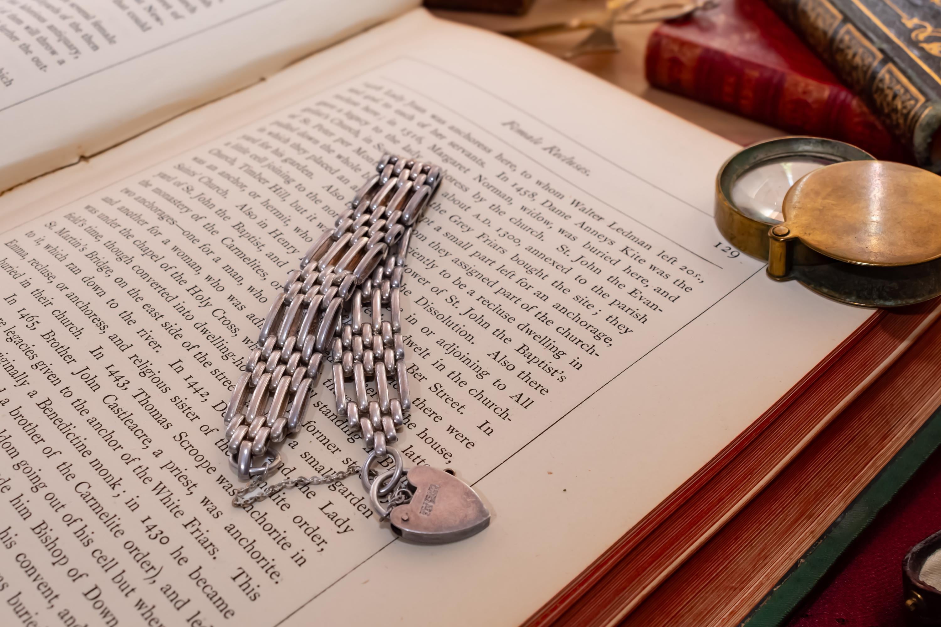 Heavy vintage sterling silver gate link bracelet featuring a safety chain and a classic heart padlock clasp, displayed on the pages of an antique text.