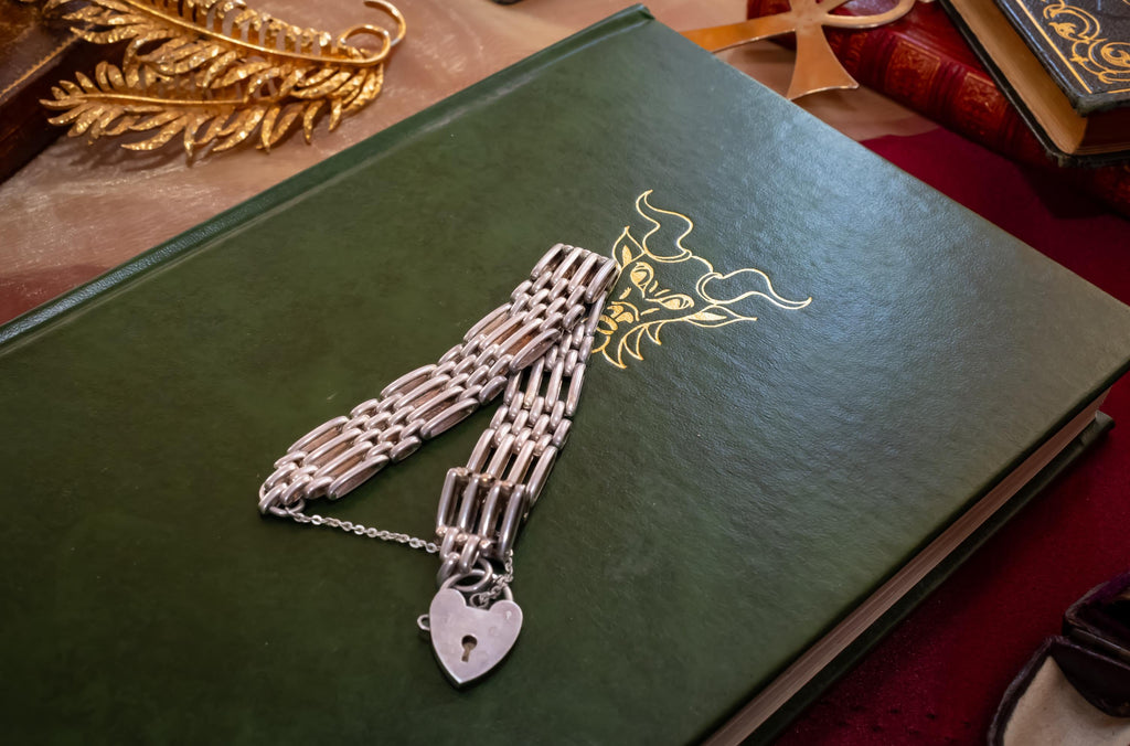 Heavy vintage sterling silver gate link bracelet featuring a safety chain and a classic heart padlock clasp, displayed on the pages of an antique text.