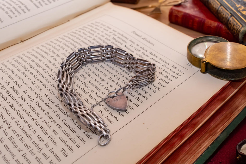 Heavy vintage sterling silver gate link bracelet featuring a safety chain and a classic heart padlock clasp, displayed on the pages of an antique text.