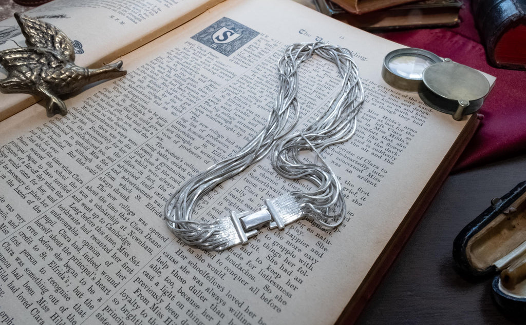 Vintage liquid sterling silver multi-strand necklace bundled together creating a heavy, fluid waterfall effect, resting on an open book.