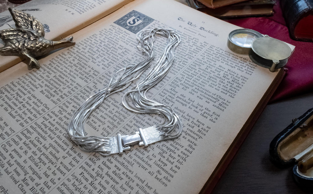 Vintage liquid sterling silver multi-strand necklace bundled together creating a heavy, fluid waterfall effect, resting on an open book.