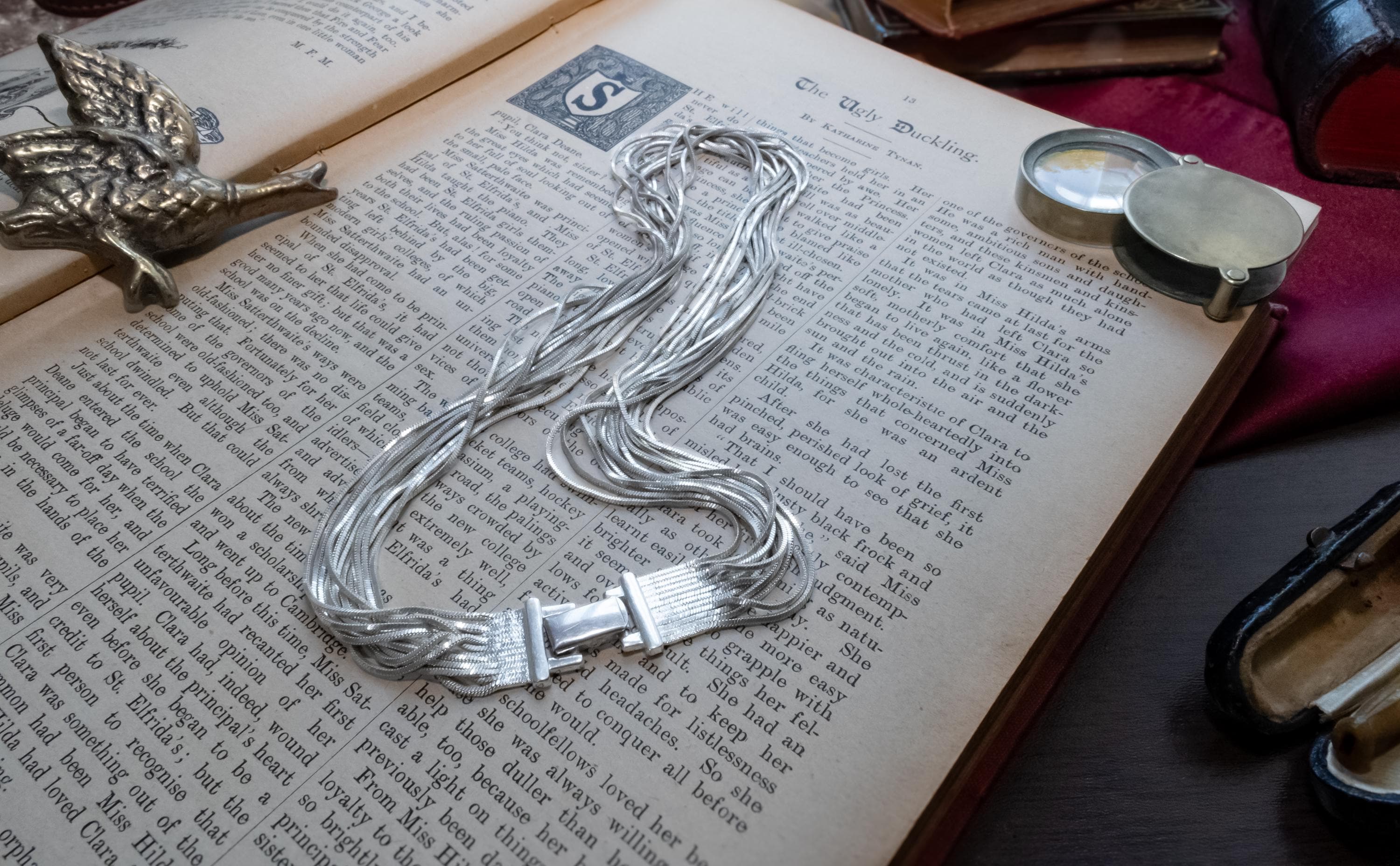 Vintage liquid sterling silver multi-strand necklace bundled together creating a heavy, fluid waterfall effect, resting on an open book.