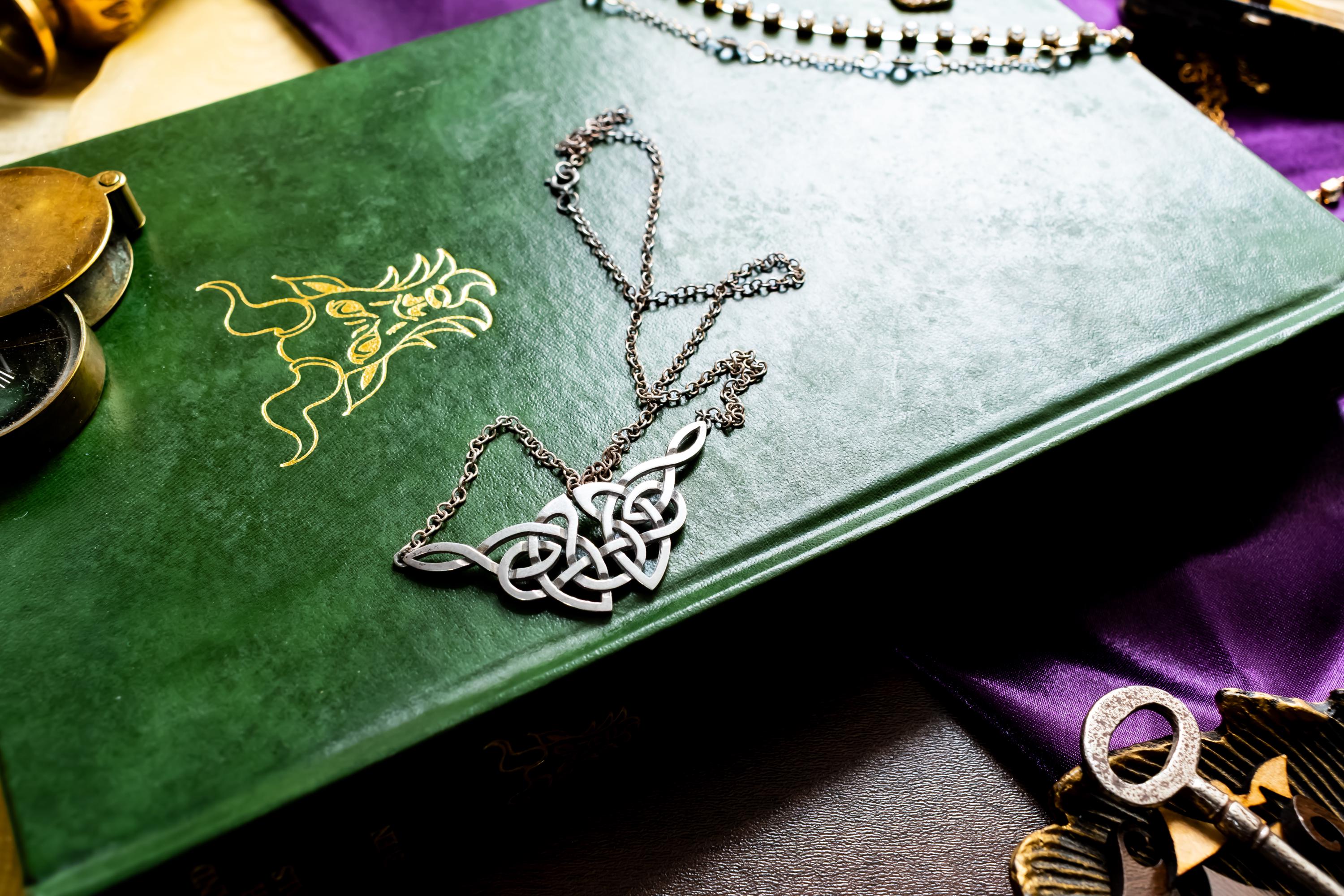 Vintage sterling silver necklace featuring a wide, intricate Celtic knot centerpiece, fully hallmarked from Edinburgh, resting on a green book.