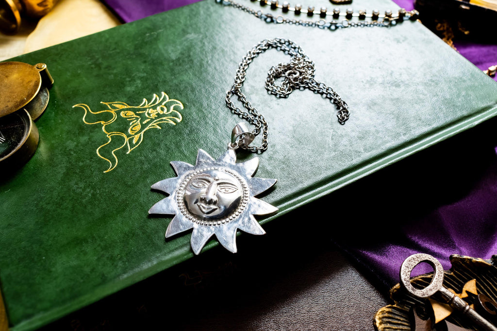 Large vintage sterling silver pendant shaped like a celestial sun with a detailed, smiling face, resting on a green antique book with gold detailing.