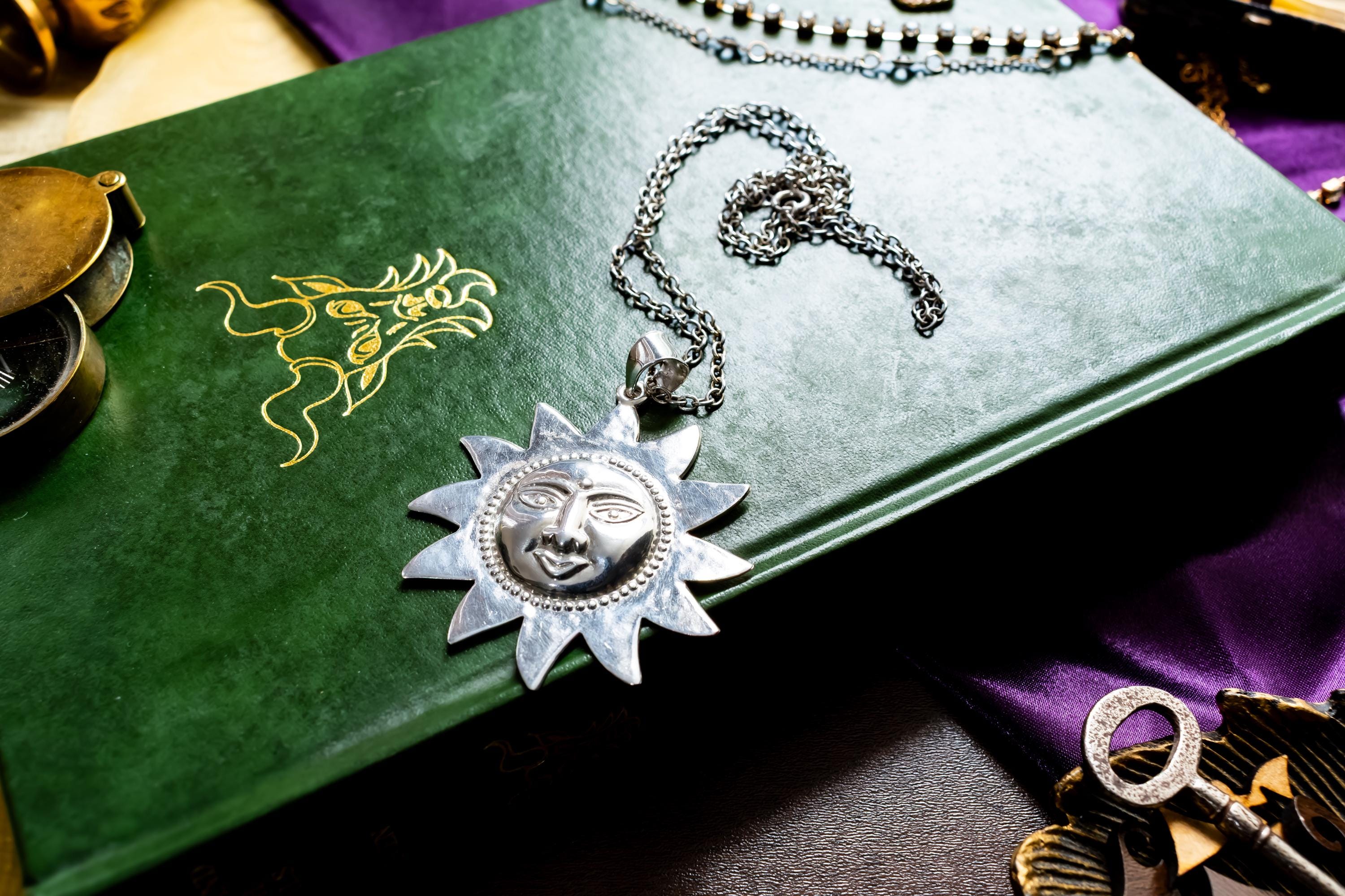 Large vintage sterling silver pendant shaped like a celestial sun with a detailed, smiling face, resting on a green antique book with gold detailing.