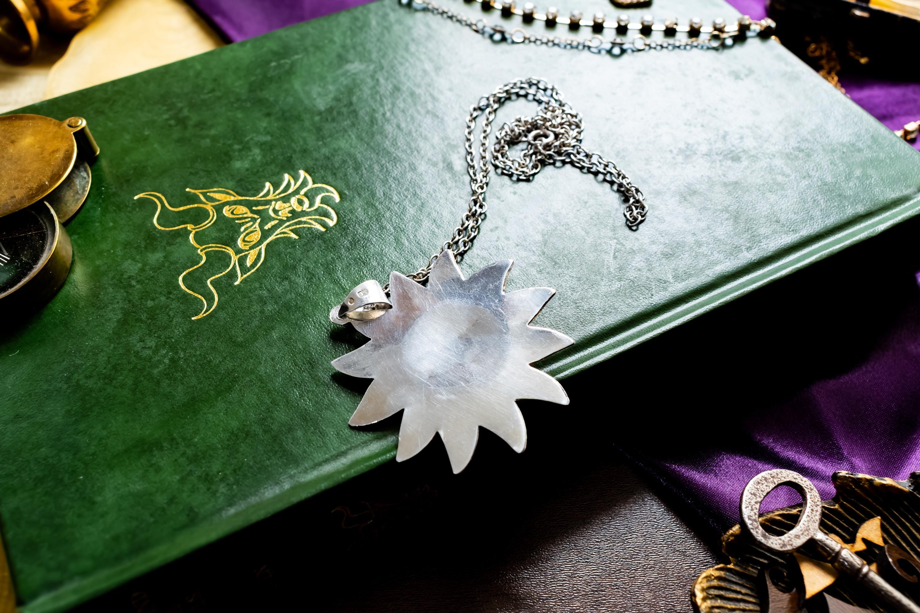 Large vintage sterling silver pendant shaped like a celestial sun with a detailed, smiling face, resting on a green antique book with gold detailing.