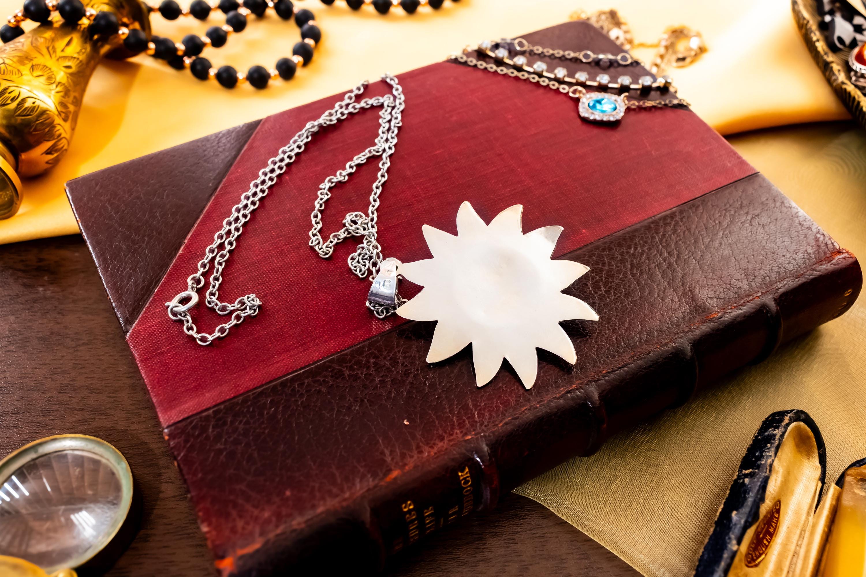 Large vintage sterling silver pendant shaped like a celestial sun with a detailed, smiling face, resting on a green antique book with gold detailing.