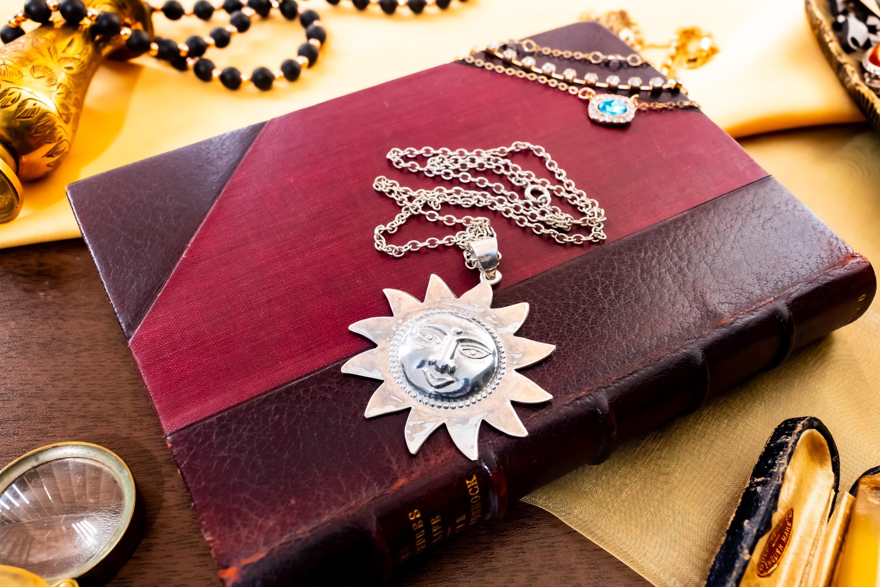 Large vintage sterling silver pendant shaped like a celestial sun with a detailed, smiling face, resting on a green antique book with gold detailing.