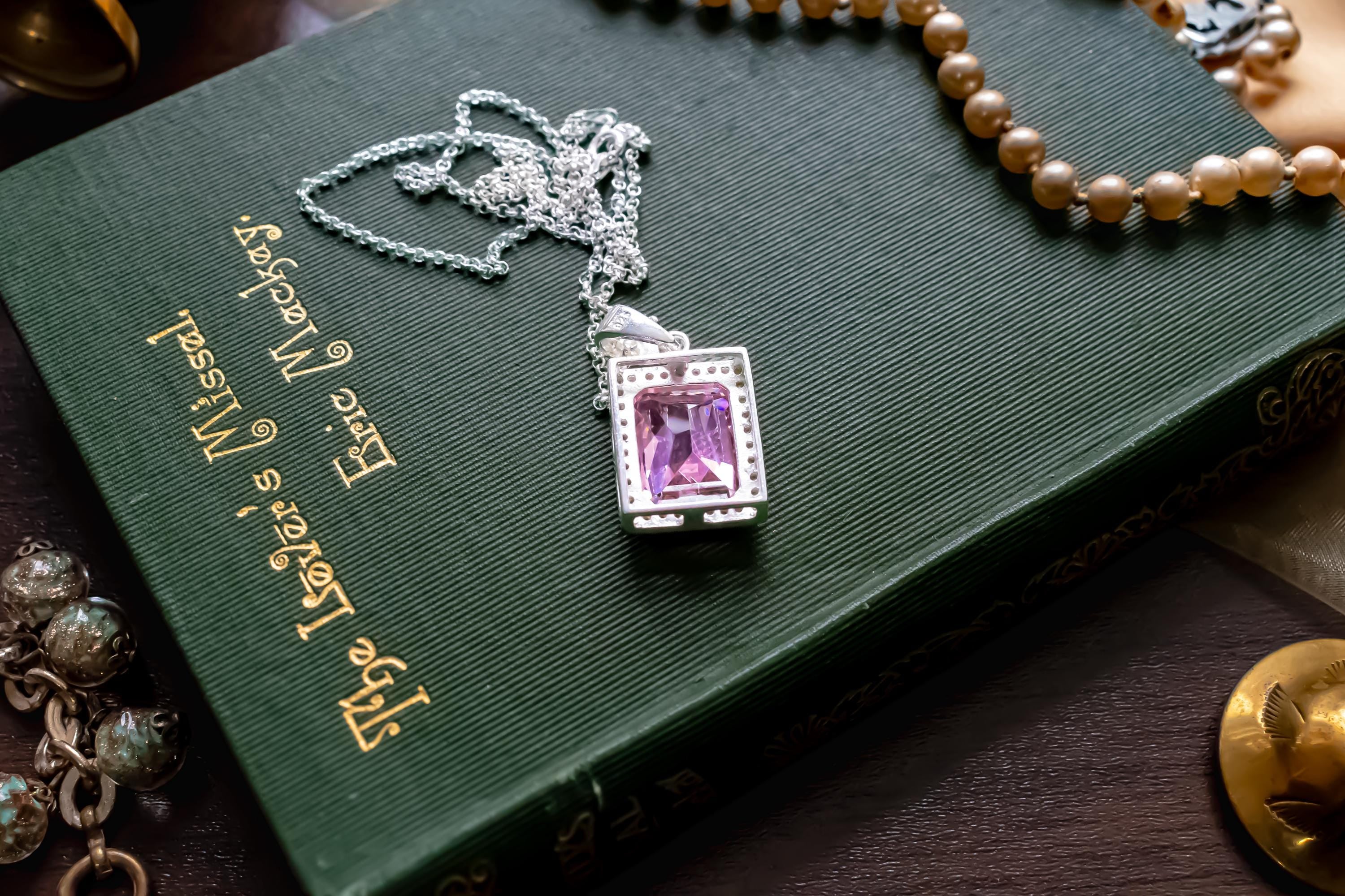 Vintage sterling silver necklace showcasing a large, vibrant emerald-cut pink topaz gemstone surrounded by smaller accent stones, on a green book.