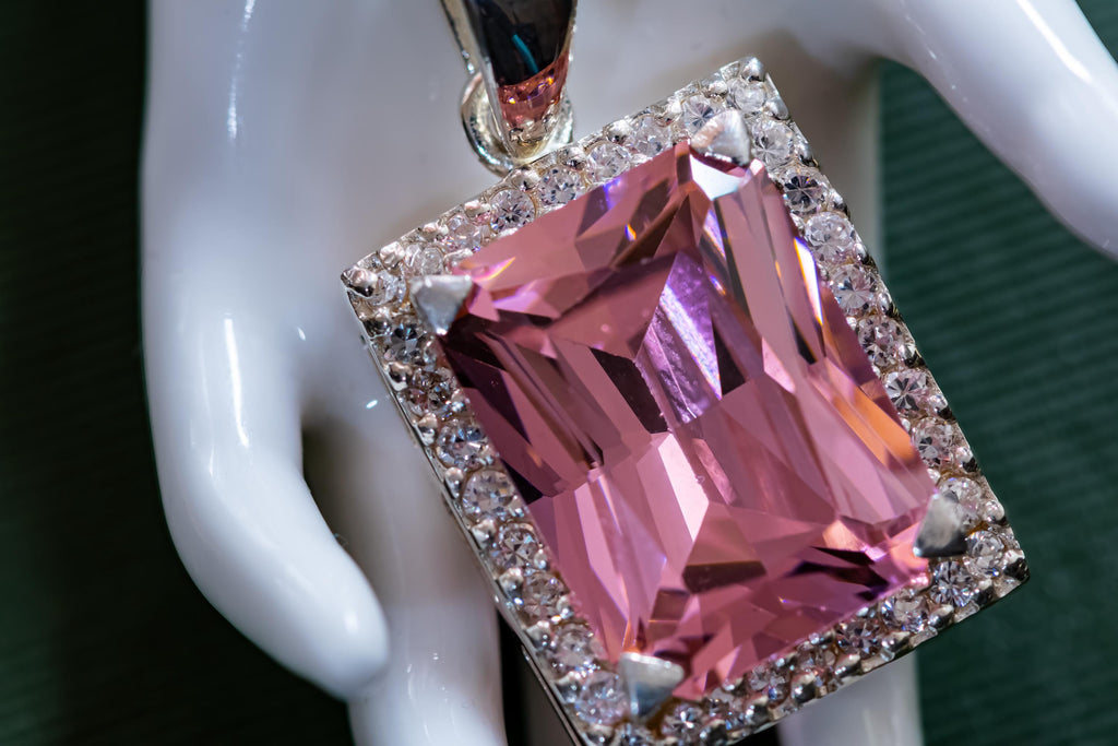 Vintage sterling silver necklace showcasing a large, vibrant emerald-cut pink topaz gemstone surrounded by smaller accent stones, on a green book.