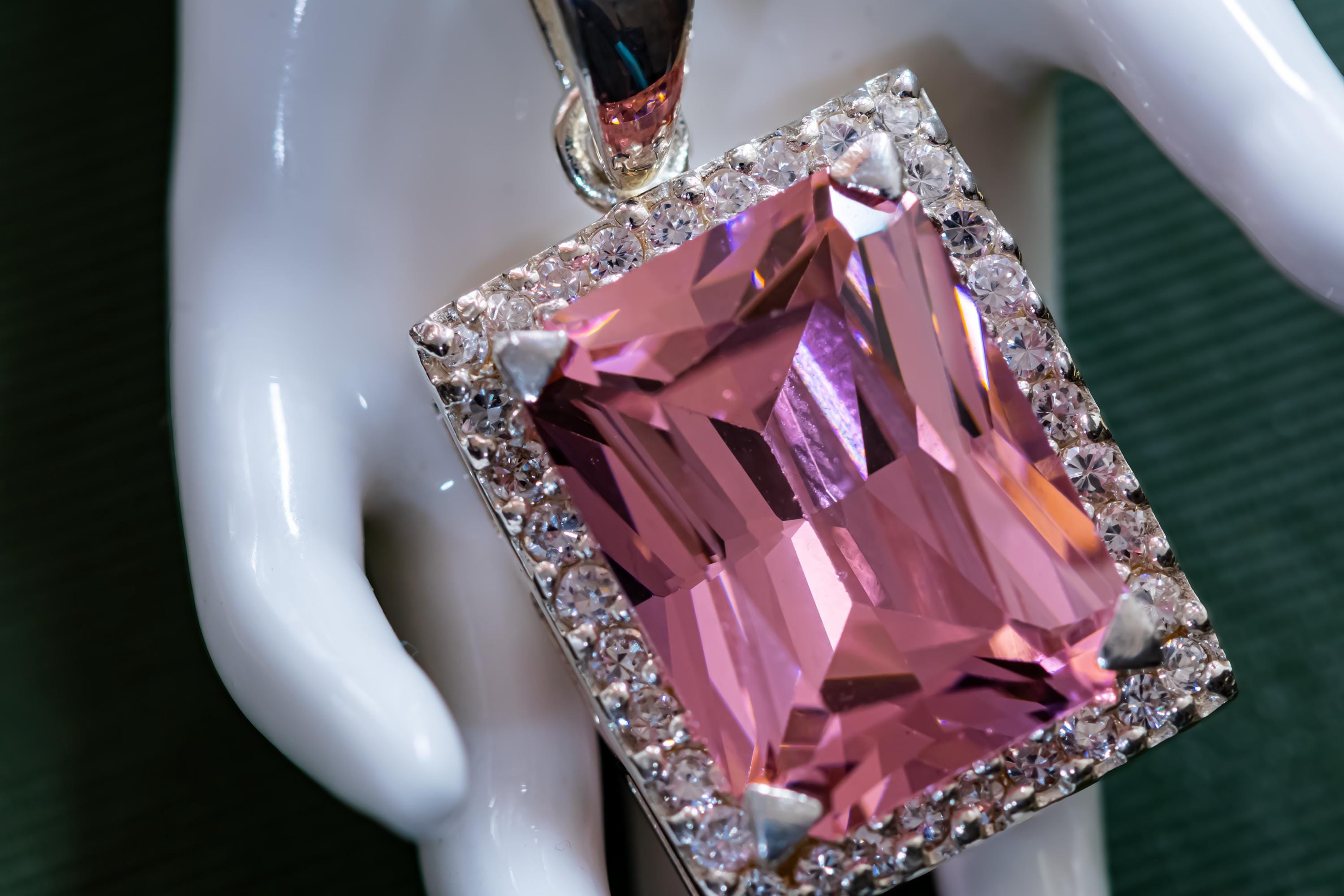 Vintage sterling silver necklace showcasing a large, vibrant emerald-cut pink topaz gemstone surrounded by smaller accent stones, on a green book.