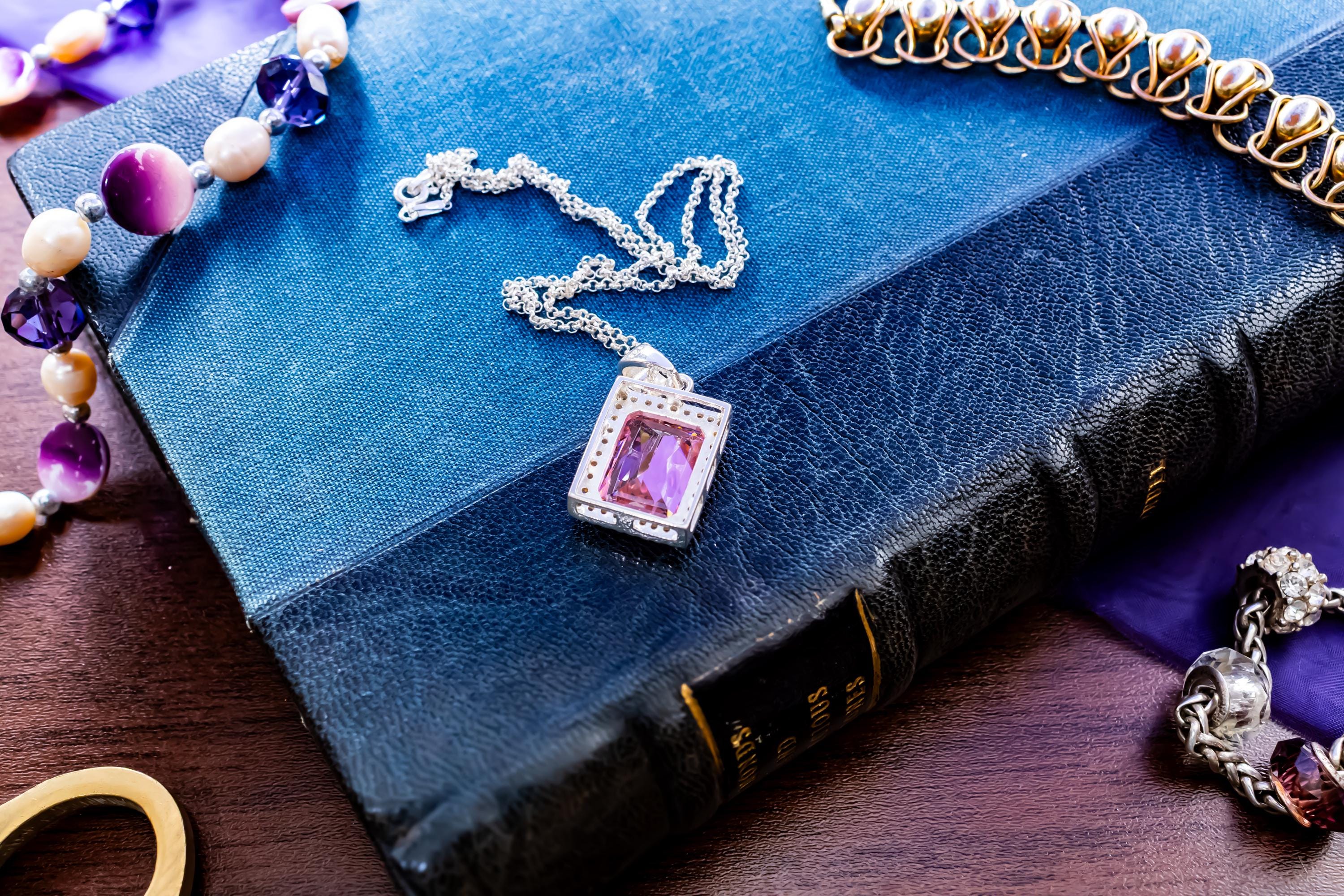 Vintage sterling silver necklace showcasing a large, vibrant emerald-cut pink topaz gemstone surrounded by smaller accent stones, on a green book.