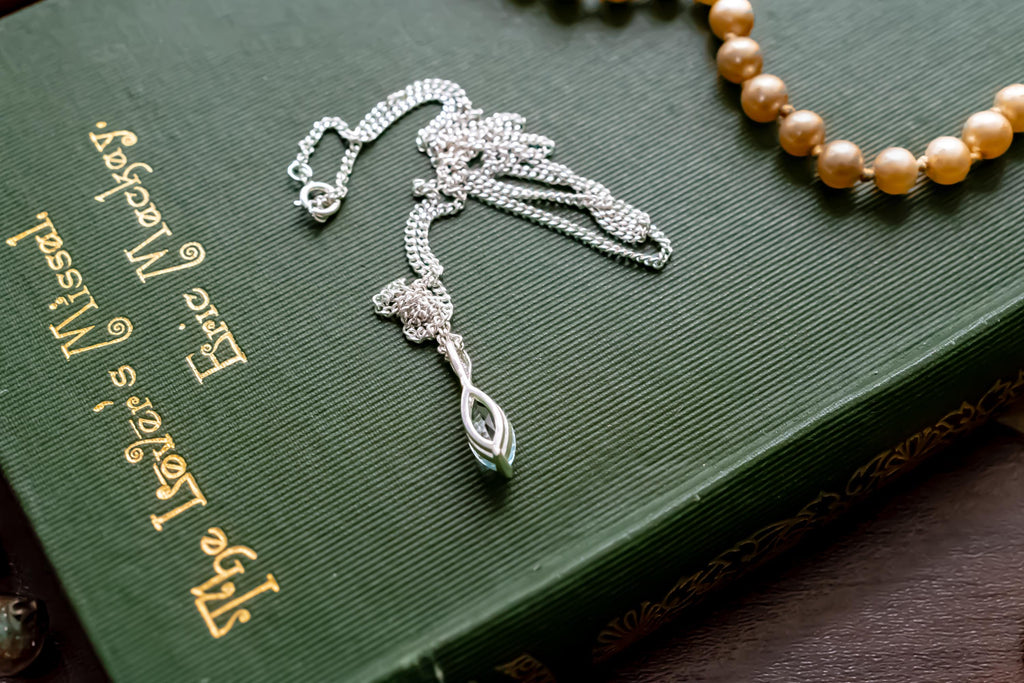 Delicate vintage 925 sterling silver necklace featuring a faceted teardrop-shaped light blue topaz gemstone, draped over a green antique book.