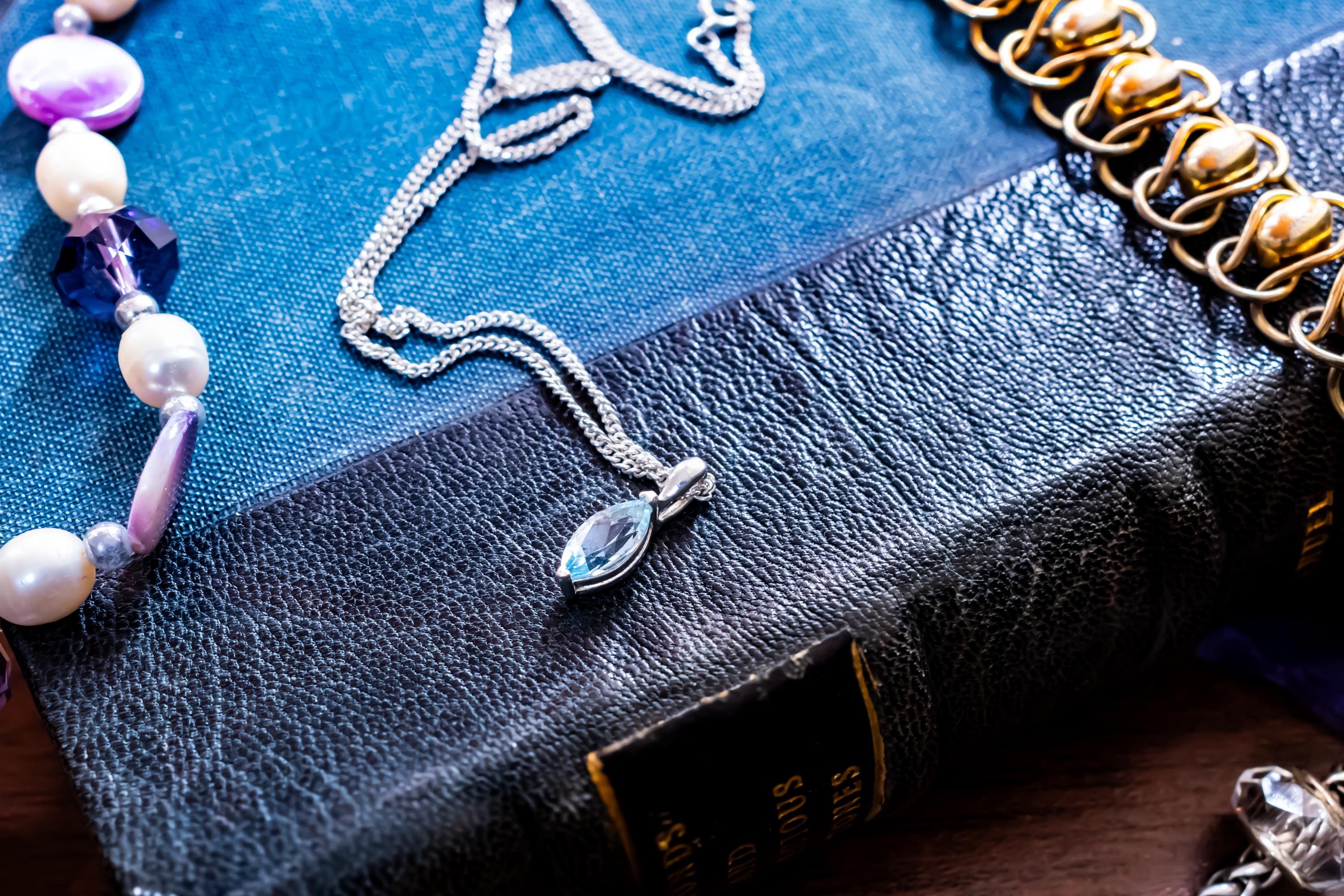 Delicate vintage 925 sterling silver necklace featuring a faceted teardrop-shaped light blue topaz gemstone, draped over a green antique book.