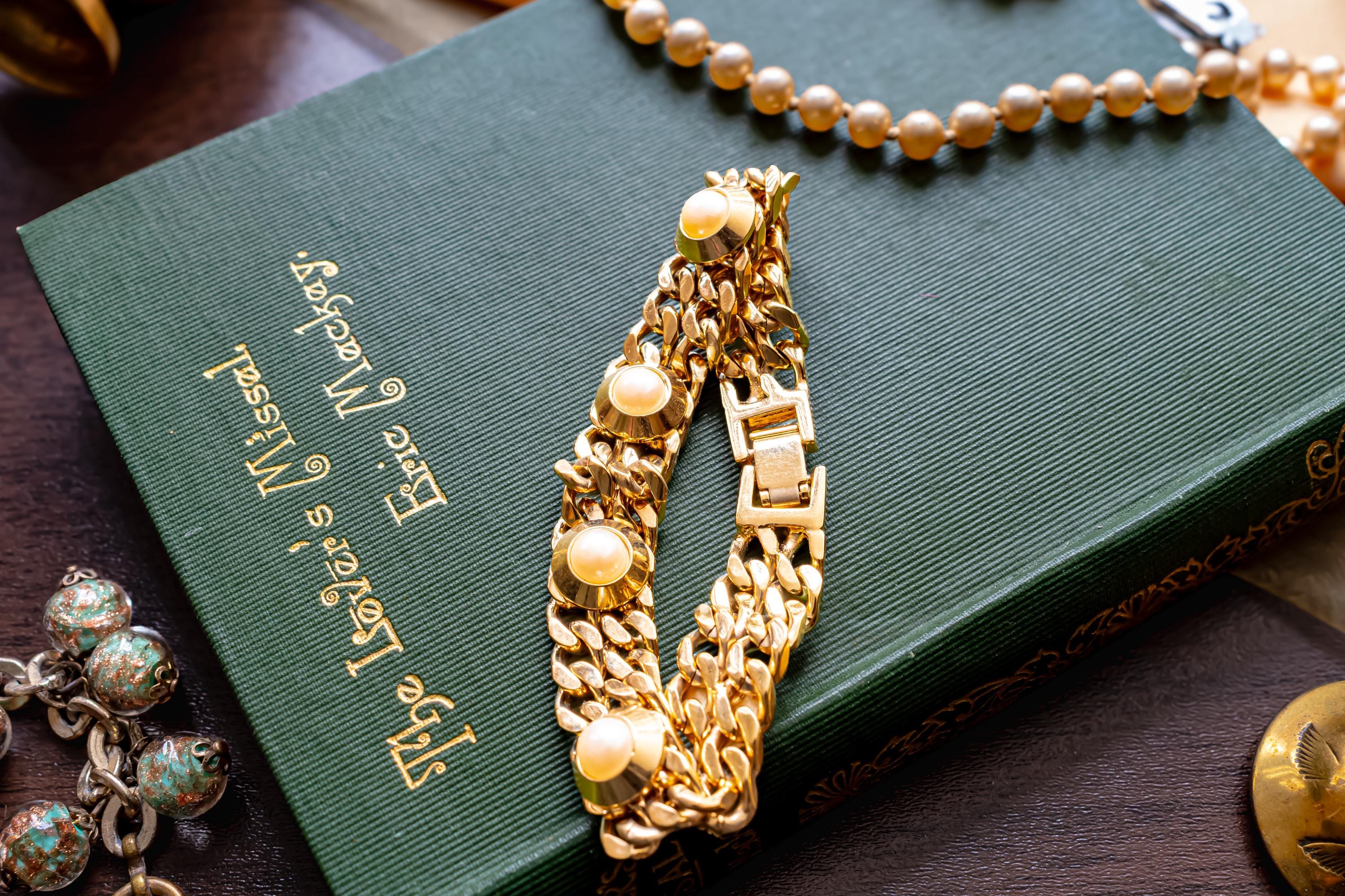 Substantial vintage chunky gold-tone curb link bracelet adorned with large faux pearls in heavy settings, resting on a green vintage book.