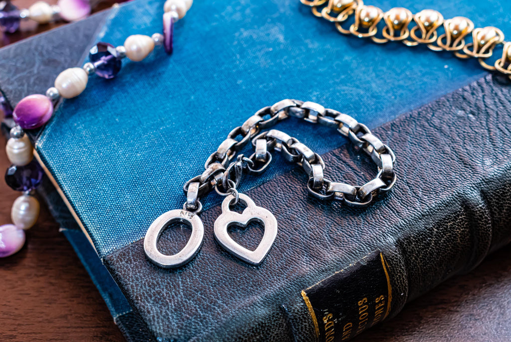 Vintage chunky sterling silver link bracelet featuring a heart charm and a toggle clasp closure, resting on an antique blue book.