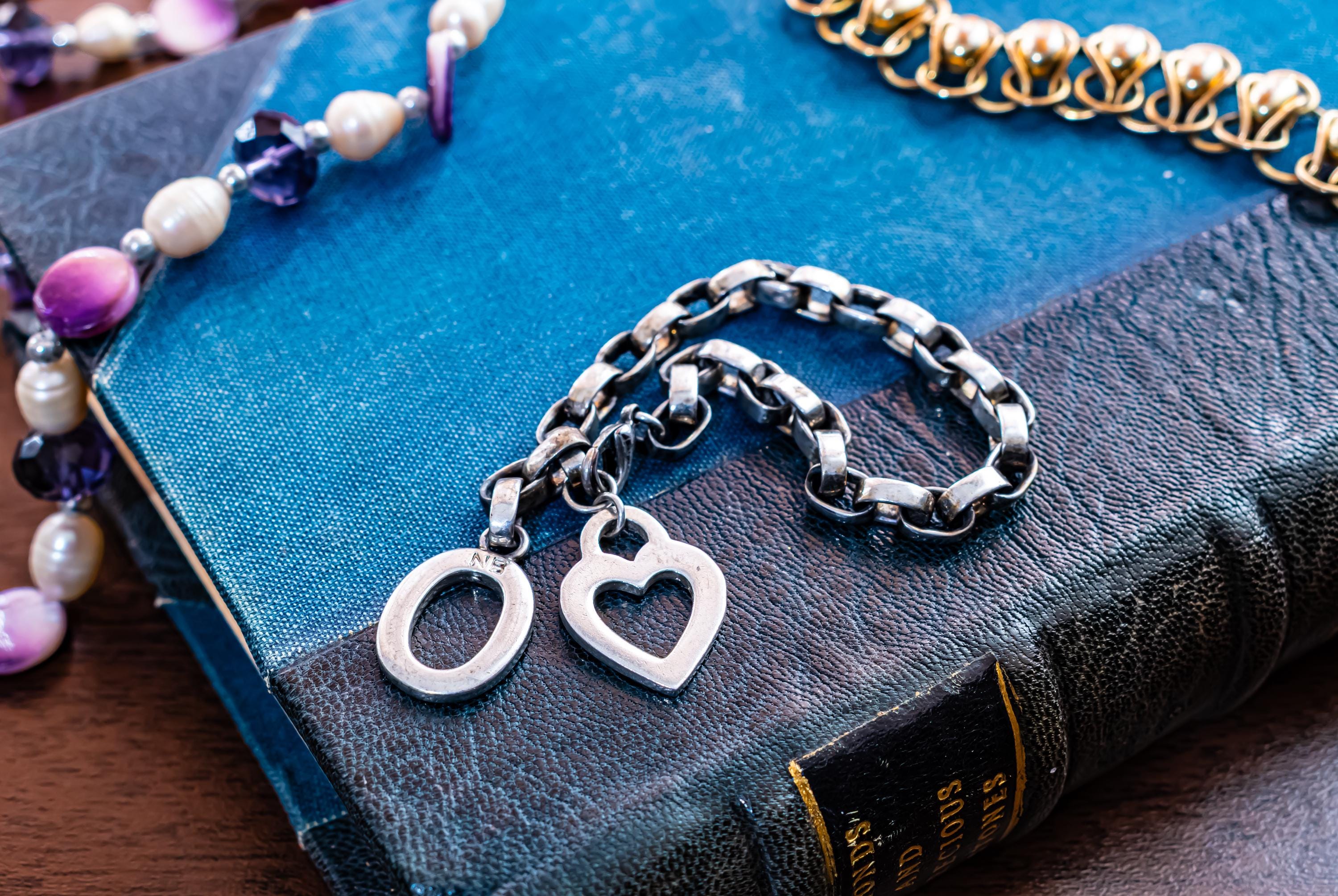 Vintage chunky sterling silver link bracelet featuring a heart charm and a toggle clasp closure, resting on an antique blue book.