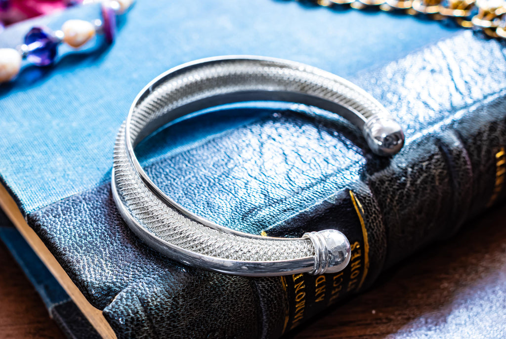 Vintage sterling silver open torque bangle with a woven mesh texture and smooth ball ends, resting on an antique book.