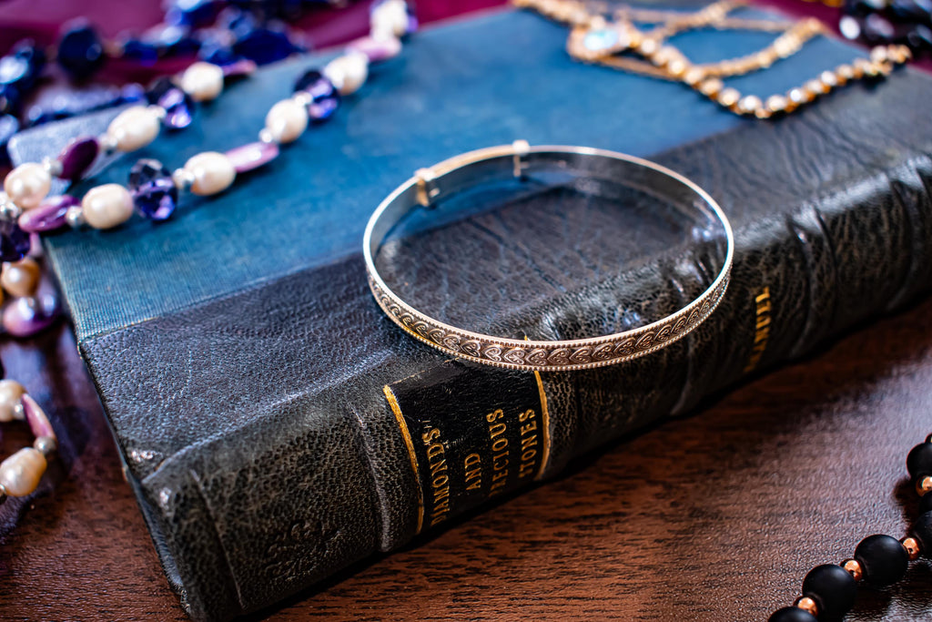 Vintage 1996 sterling silver flexible bangle with intricate engraved patterns along the band, sitting on a vintage blue book.