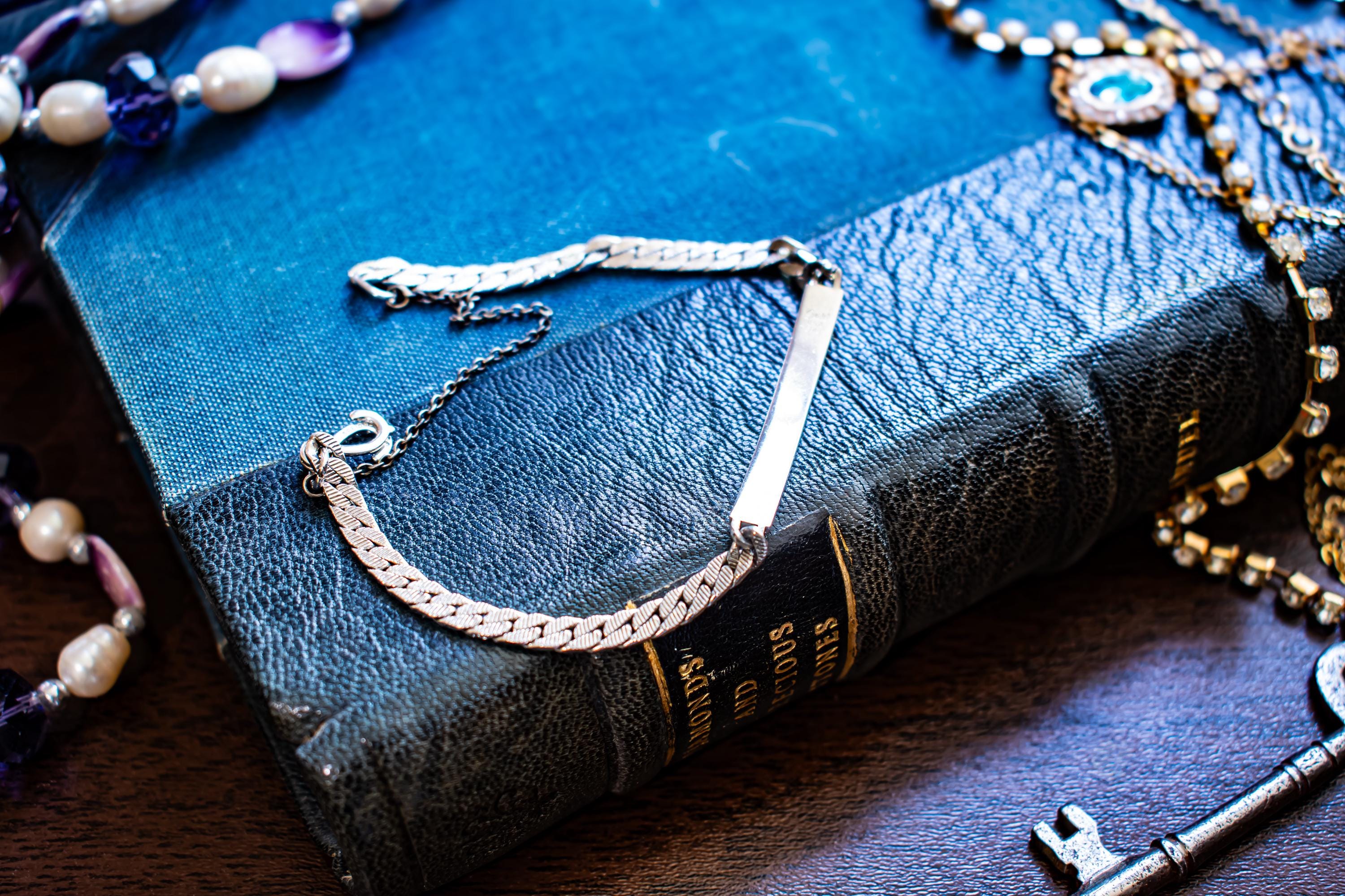 Vintage silver-tone Speidel USA ID bracelet featuring a blank rectangular plate, interlocking sister hook clasp, and safety chain, resting on an antique book.