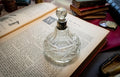 An antique heavy cut glass scent bottle with a sterling silver collar and crystal stopper, sitting on an open vintage book surrounded by dark academia props