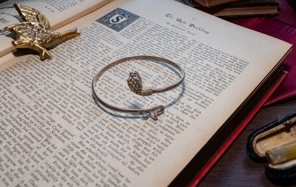vintage 925 sterling silver bypass bangle featuring two sculpted serpent heads, resting beautifully on the text of an open antique book.