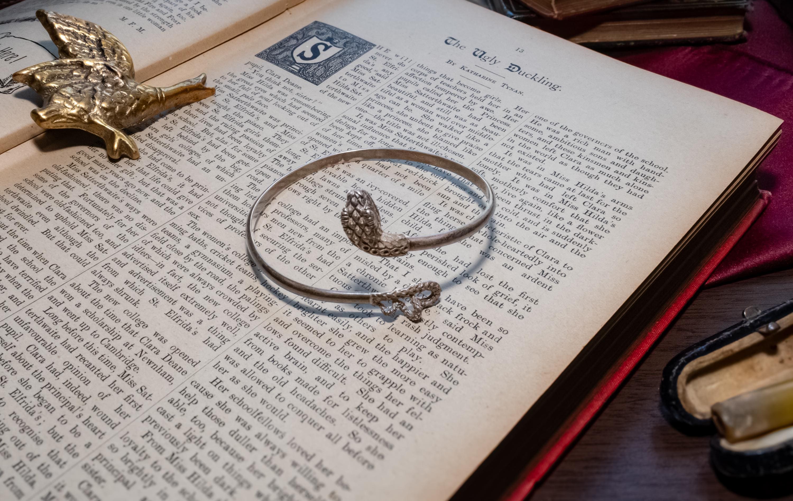 vintage 925 sterling silver bypass bangle featuring two sculpted serpent heads, resting beautifully on the text of an open antique book.