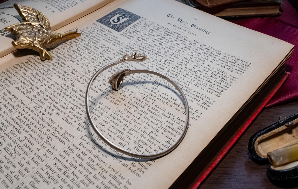 vintage 925 sterling silver bypass bangle featuring two sculpted serpent heads, resting beautifully on the text of an open antique book.