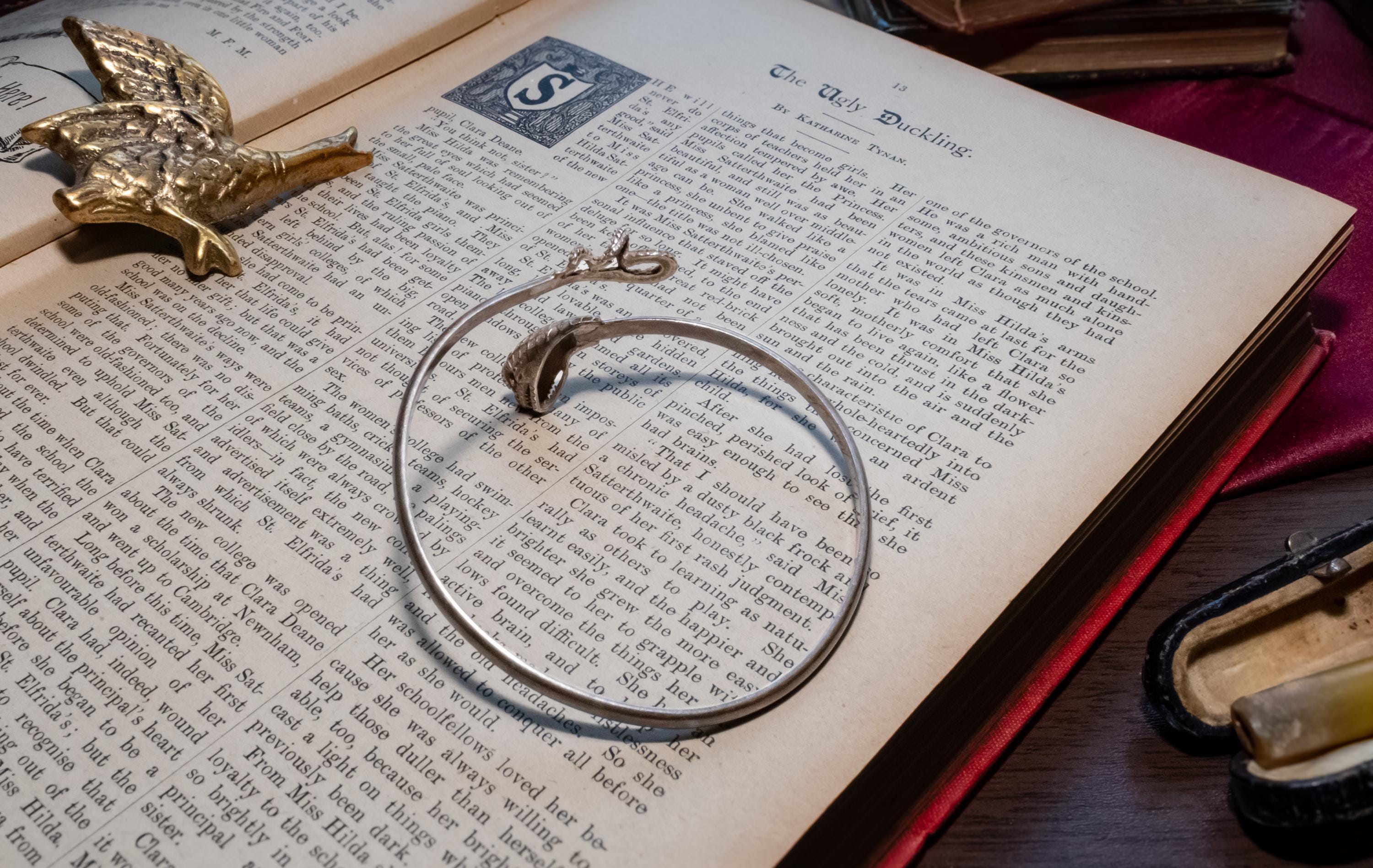 vintage 925 sterling silver bypass bangle featuring two sculpted serpent heads, resting beautifully on the text of an open antique book.