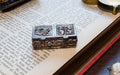 An ornate silver-toned metal keepsake box with floral and fruit motifs, resting on the pages of an open vintage book.