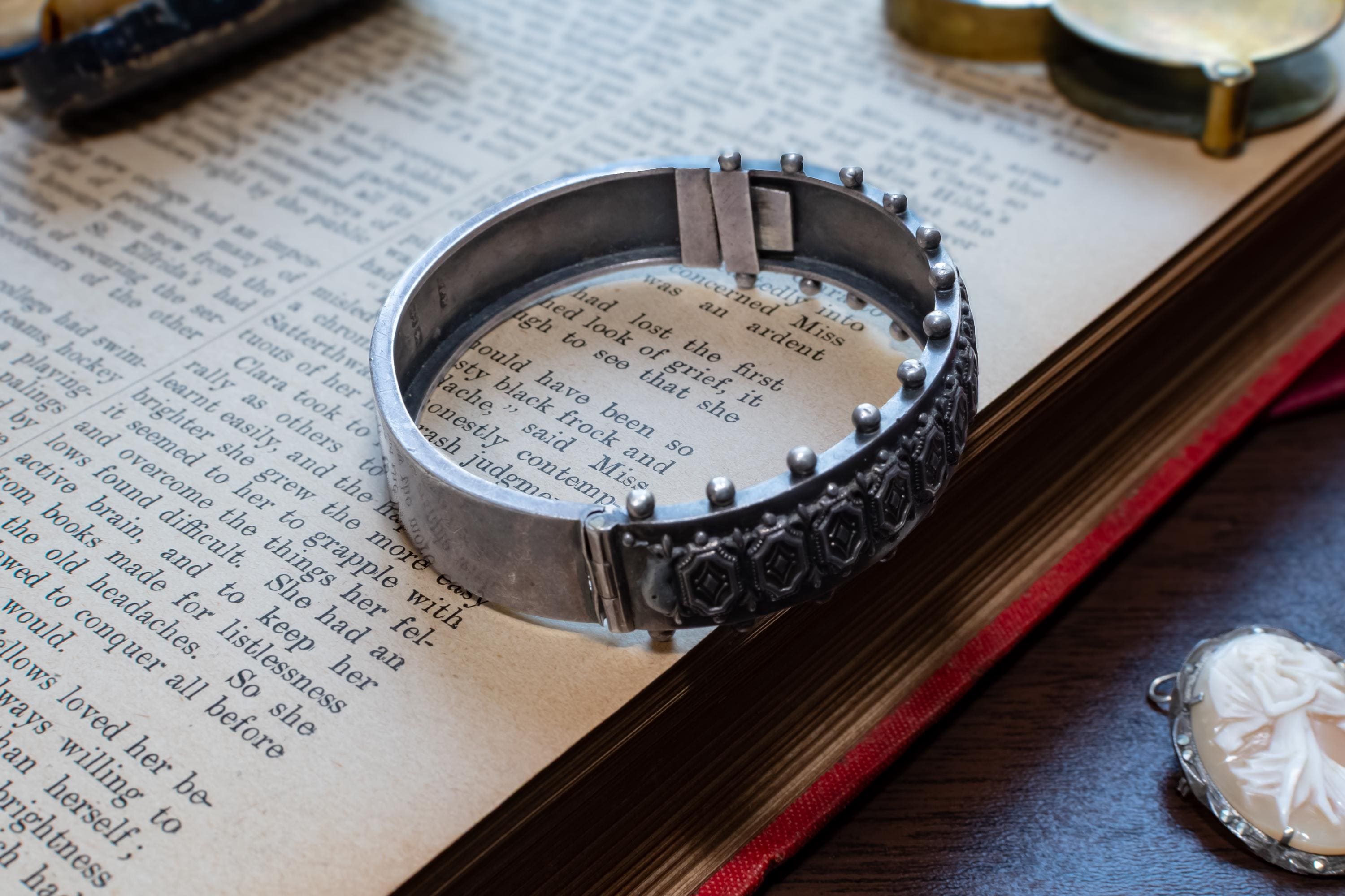 An antique 1883 heavy sterling silver cuff bracelet by Robert James Dick featuring intricate geometric and beadwork detailing, resting on the text of an open vintage book.