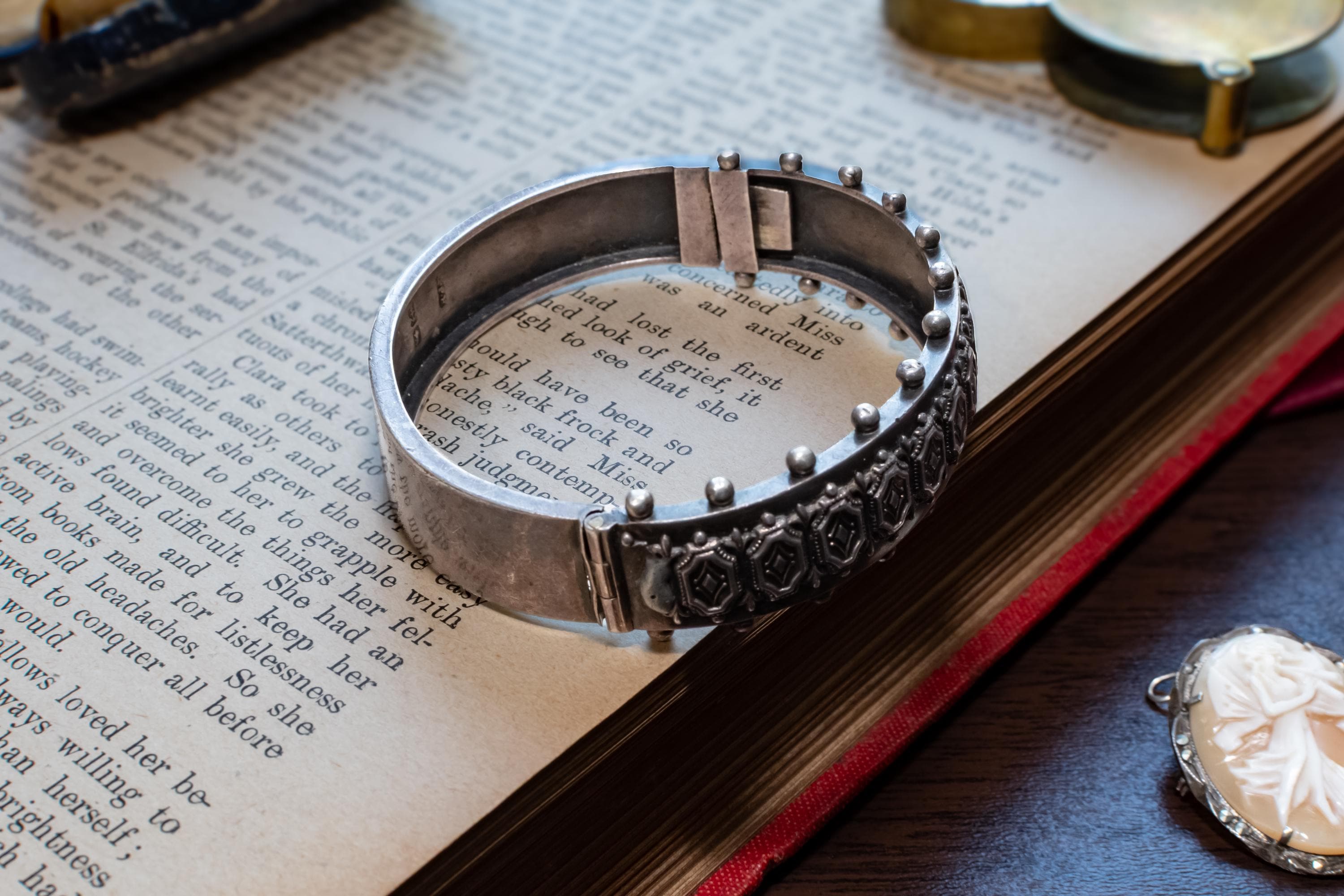 An antique 1883 heavy sterling silver cuff bracelet by Robert James Dick featuring intricate geometric and beadwork detailing, resting on the text of an open vintage book.