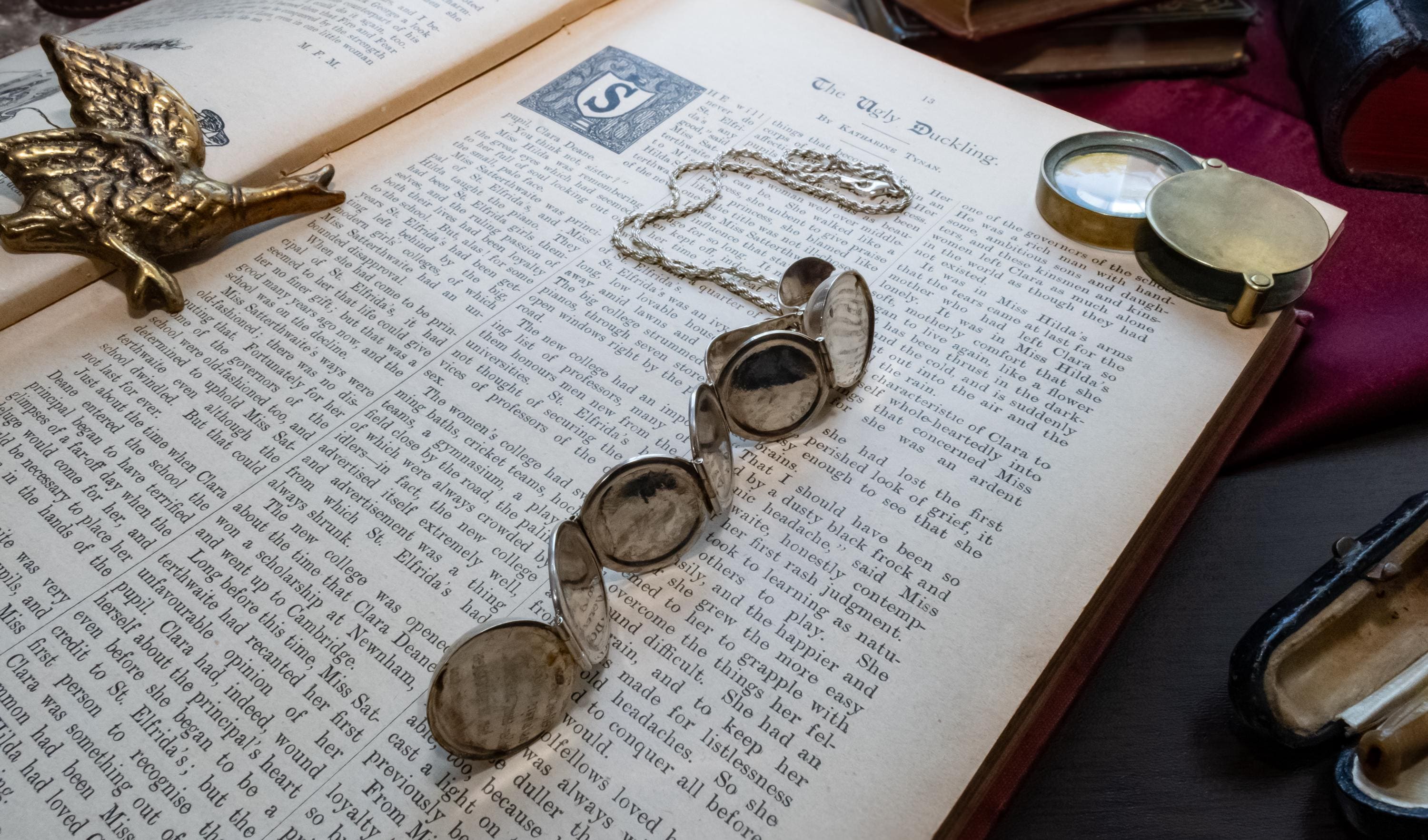 An antique silver ribbed sphere locket resting on an open vintage book. The first image shows the locket closed as a solid ball. The second image shows the locket mechanically unfolded into an accordion of six circular picture frames, lying across the text.