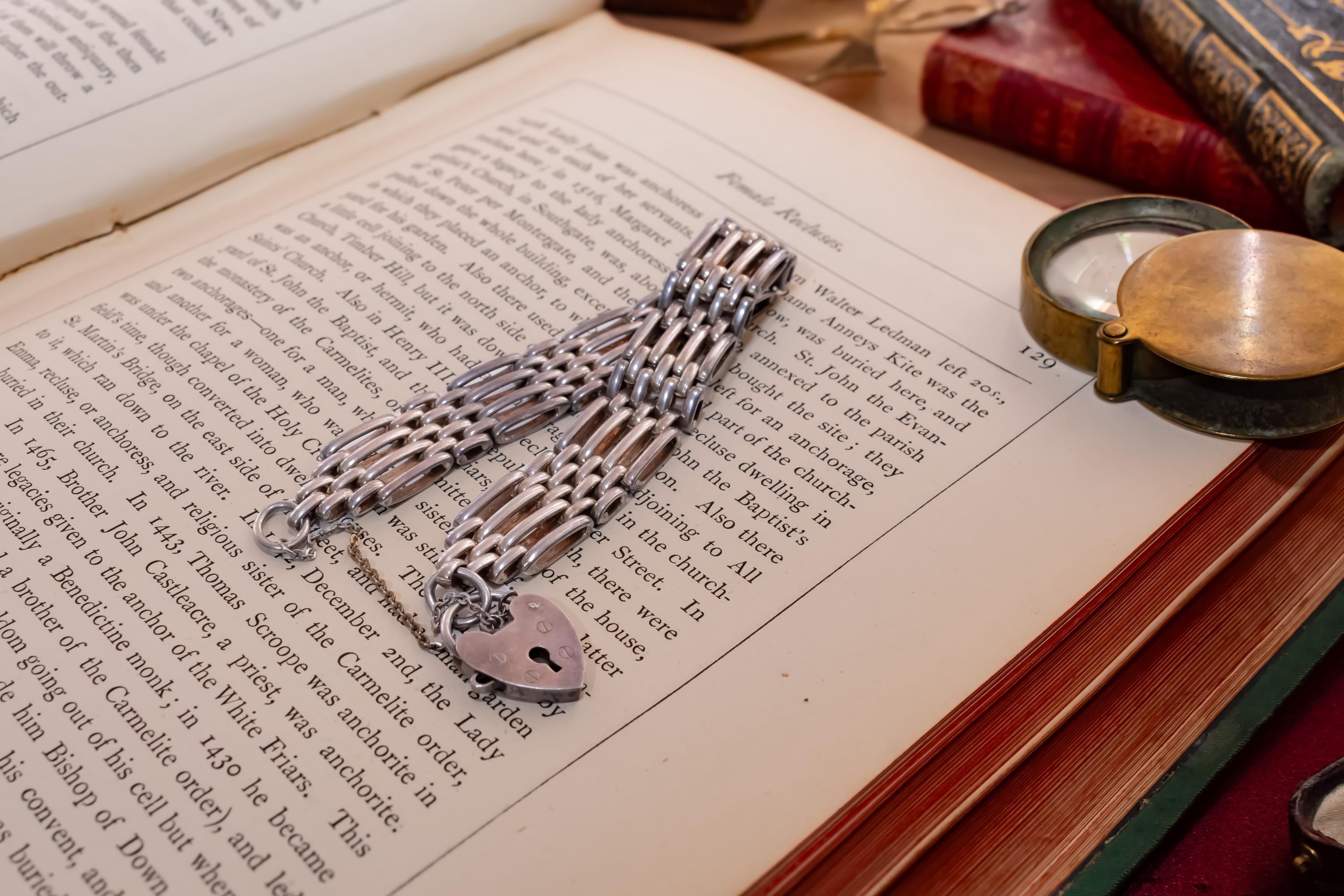 Heavy vintage sterling silver gate link bracelet featuring a safety chain and a classic heart padlock clasp, displayed on the pages of an antique text.