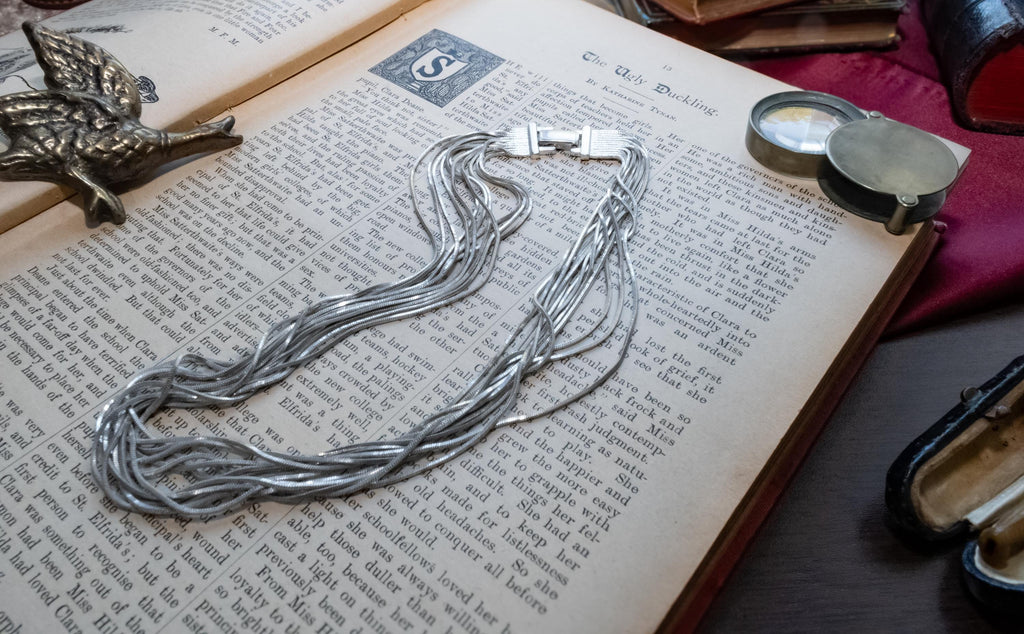 Vintage liquid sterling silver multi-strand necklace bundled together creating a heavy, fluid waterfall effect, resting on an open book.